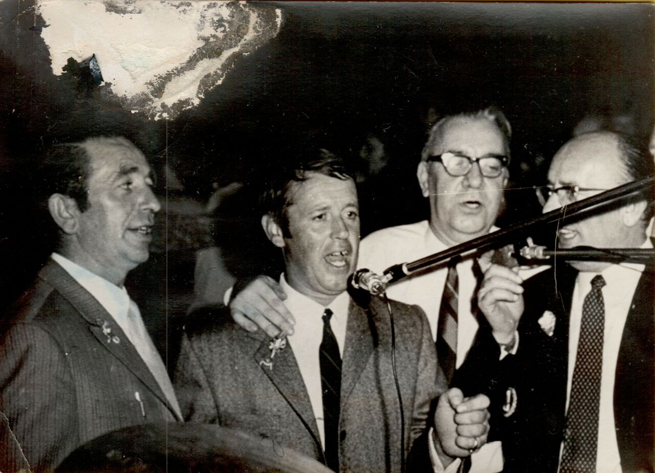 Four men in suits singing together into microphones at a New Year's Eve party.