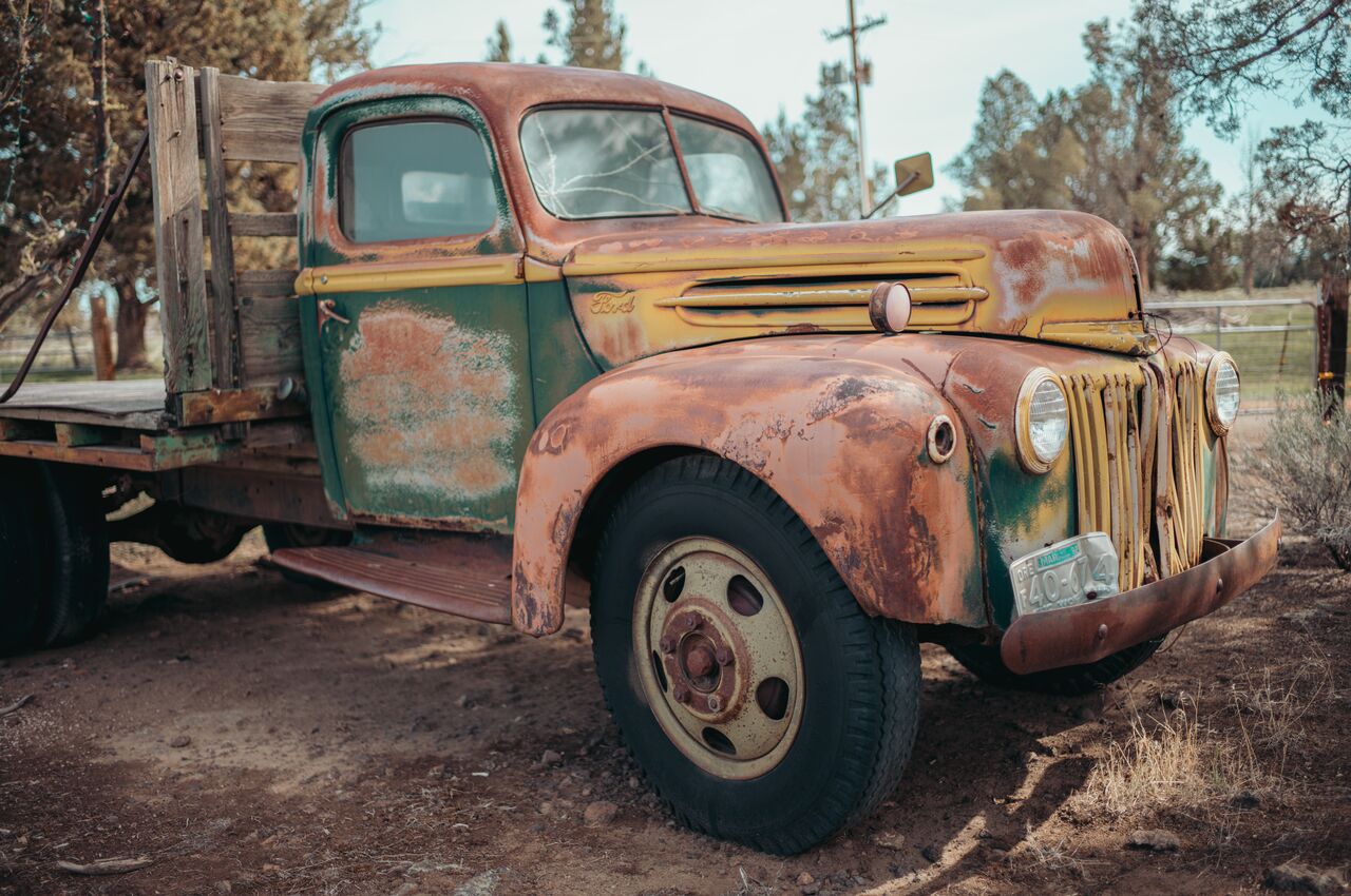 Rusted Ford truck Old rusted Ford truck parked on dirt, with faded paint and wooden flatbed in the back.