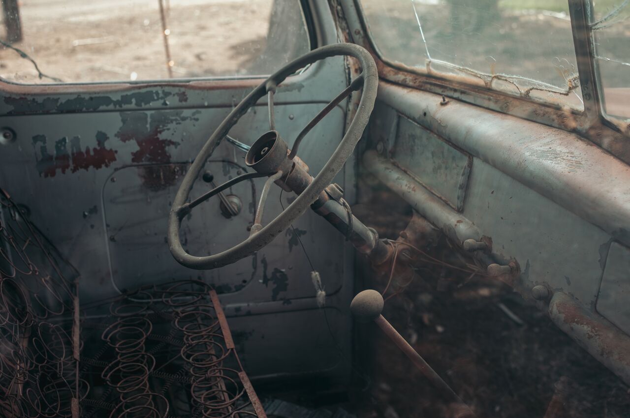Vintage truck interior Rusty steering wheel and exposed seat springs inside an old, abandoned truck with cracked windows.