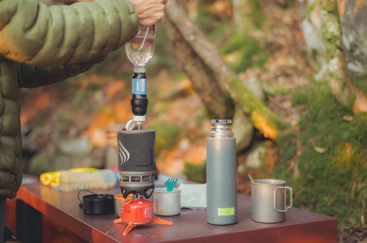 A person filtering water and pouring it into a pot on a camp stove.