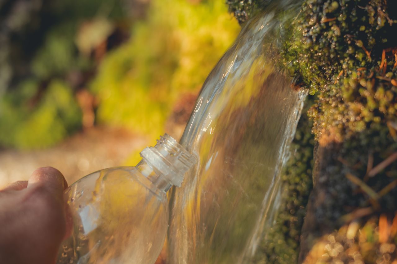 A close-up of a water bottle being filled from a stream.