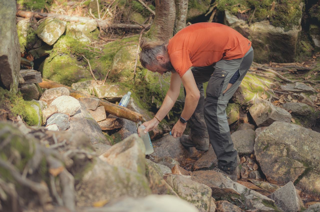 A hiker filling a water bottle from a small stream.