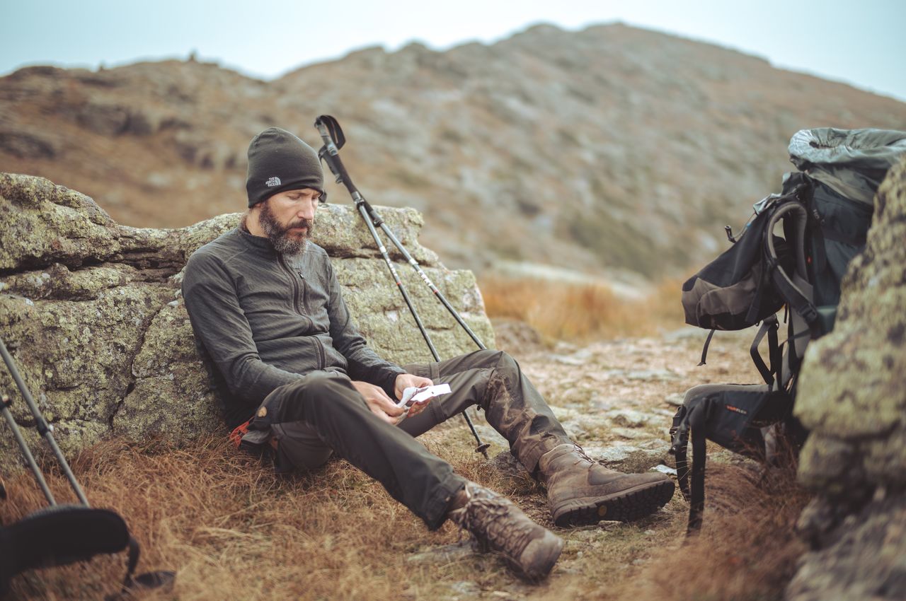 A hiker seated on the ground, looking deflated, eating some food to regain energy.