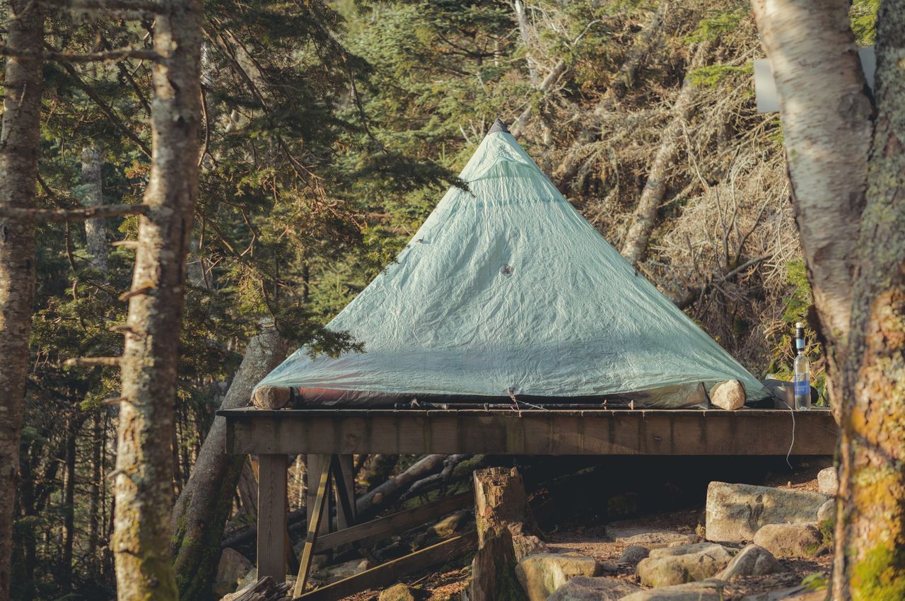 A pyramid tent set on a wooden platform, surrounded by trees and rocks.