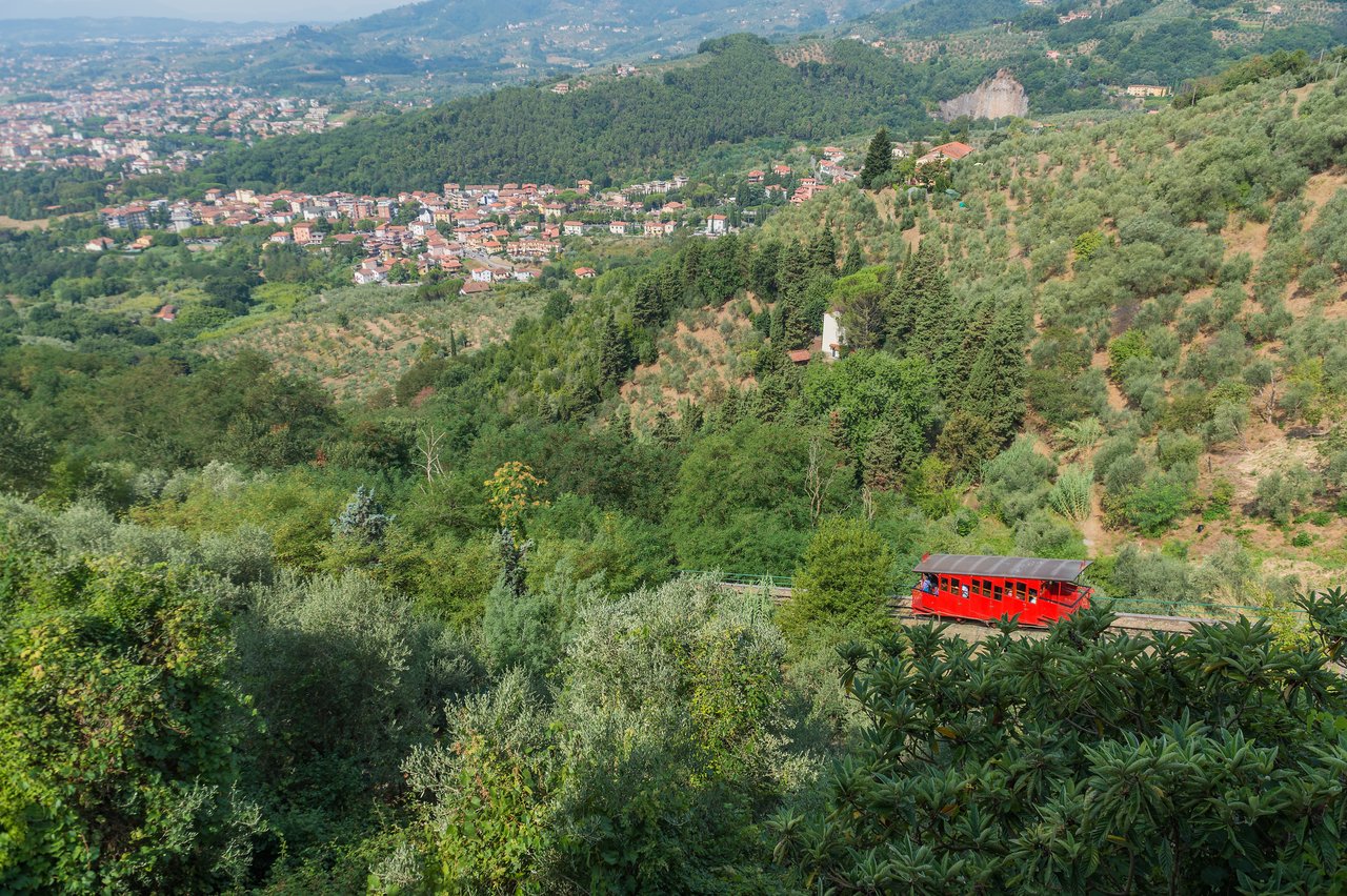 Funicular at Montecatini Alto A red funicular railway car travels up a hillside surrounded by green vegetation near Montecatini Alto, Italy.