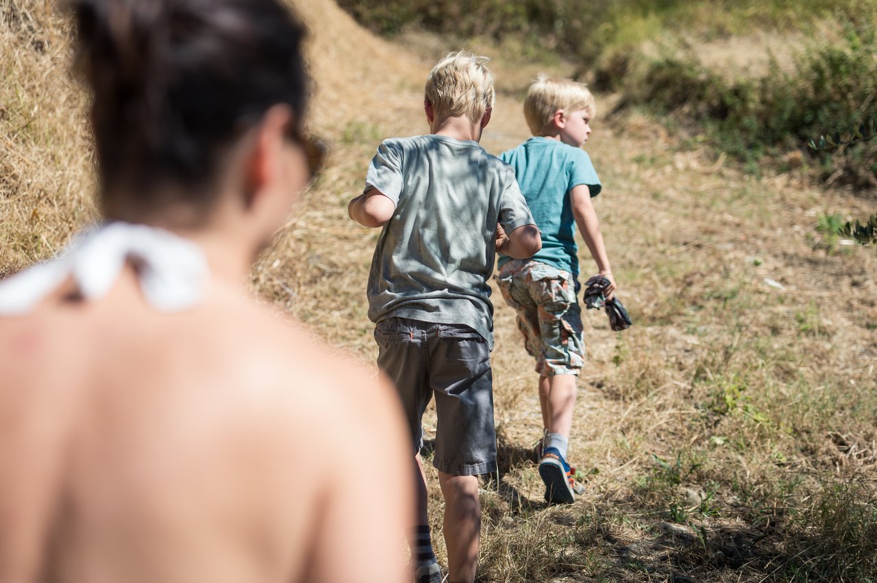 Two children walk up a dry, grassy hill while an adult follows closely behind.