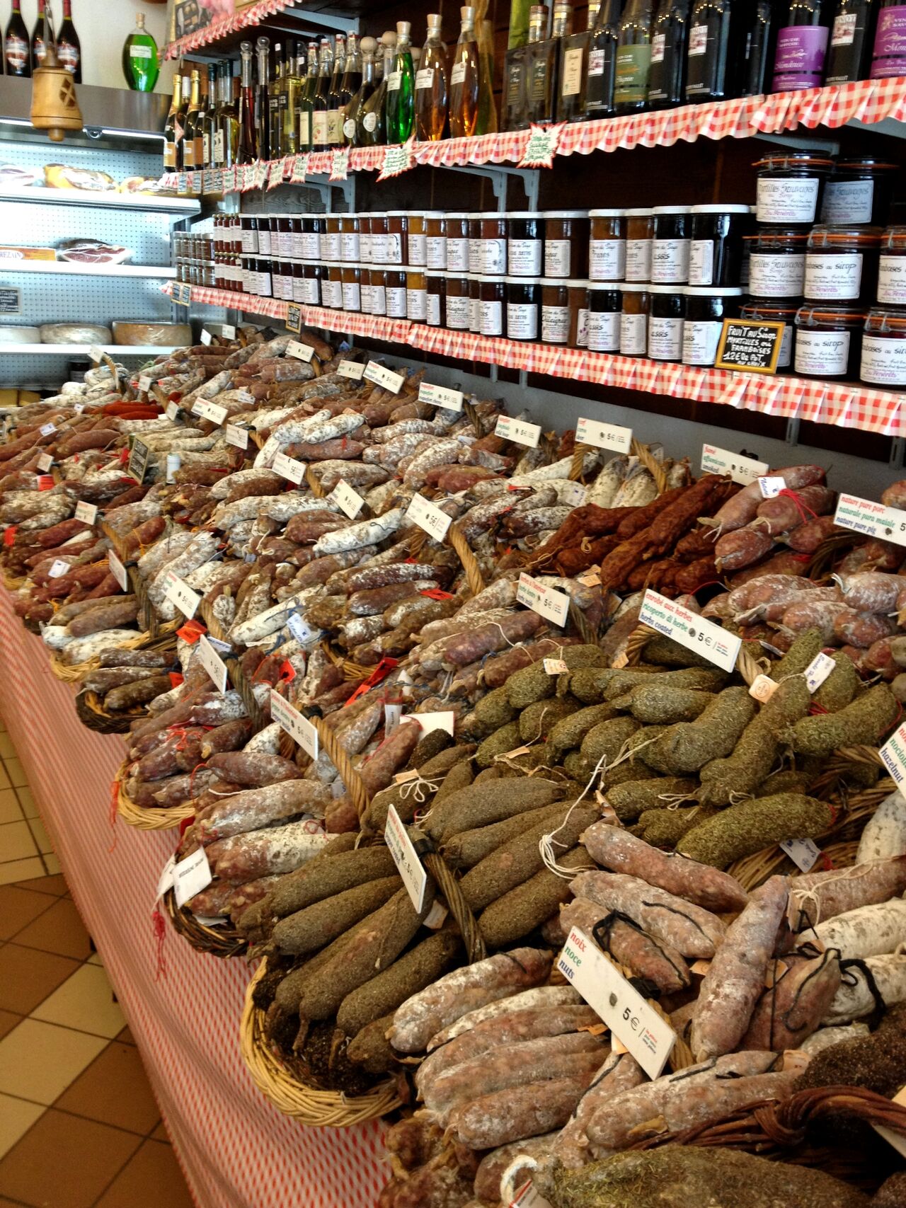 A market display with various cured sausages in baskets, labeled with prices.
