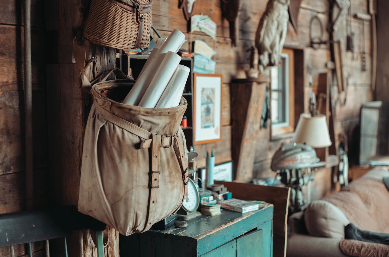 A worn canvas bag filled with rolled papers hangs on a wooden wall inside a rustic barn-like space.