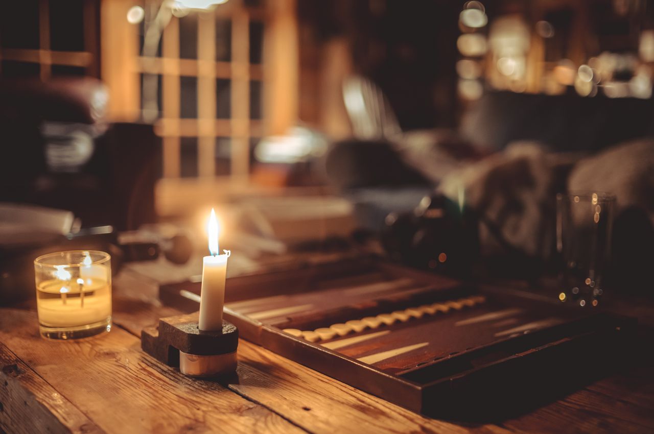 A backgammon board on a wooden table, accompanied by candles that cast a warm glow.