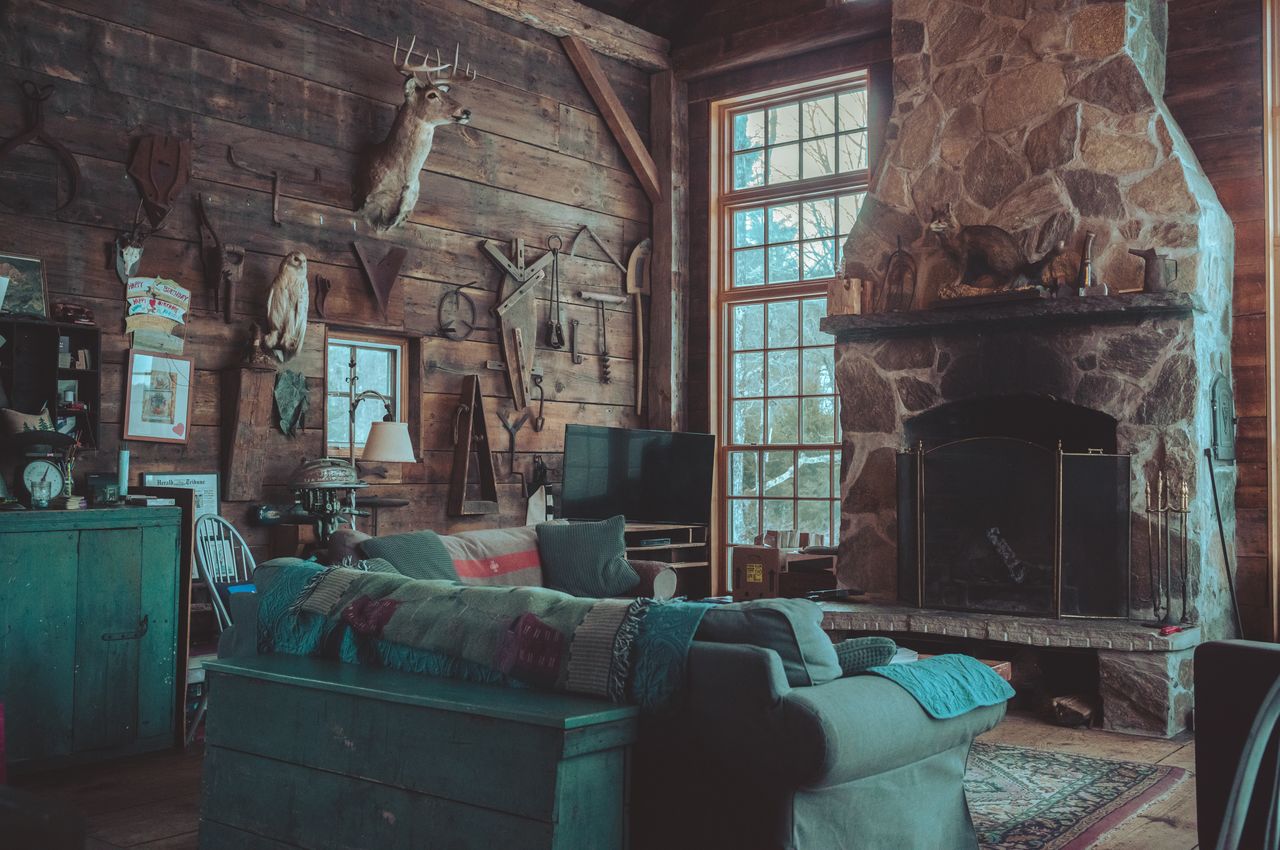 The living room is housed in an old wooden barn, featuring tall windows, a large central fireplace, and an abundance of decorations adorning the walls.