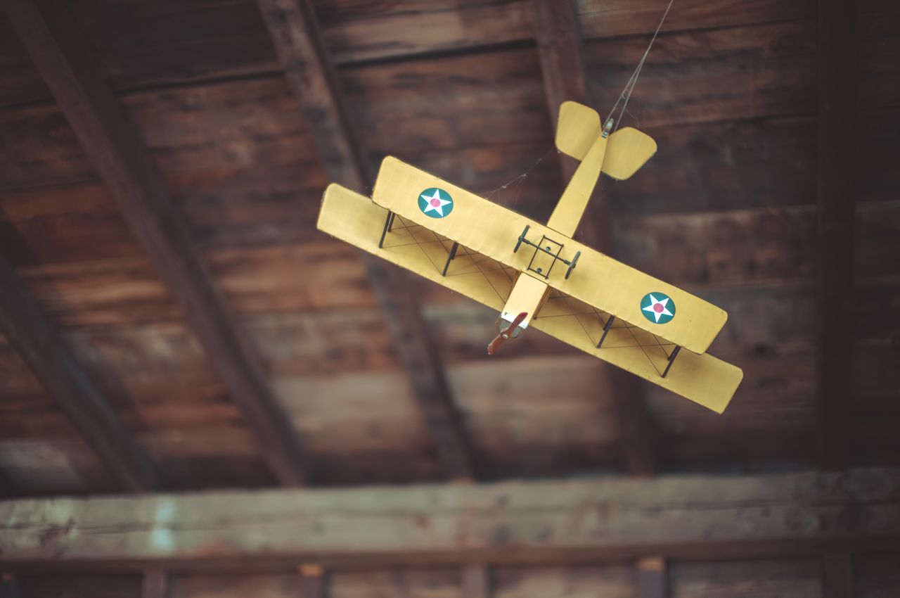 A model plane with a 3-foot or 90-centimeter wingspan hangs from dark wooden beams on the ceiling. It's an antique biplane with double-stacked wings in bright yellow.