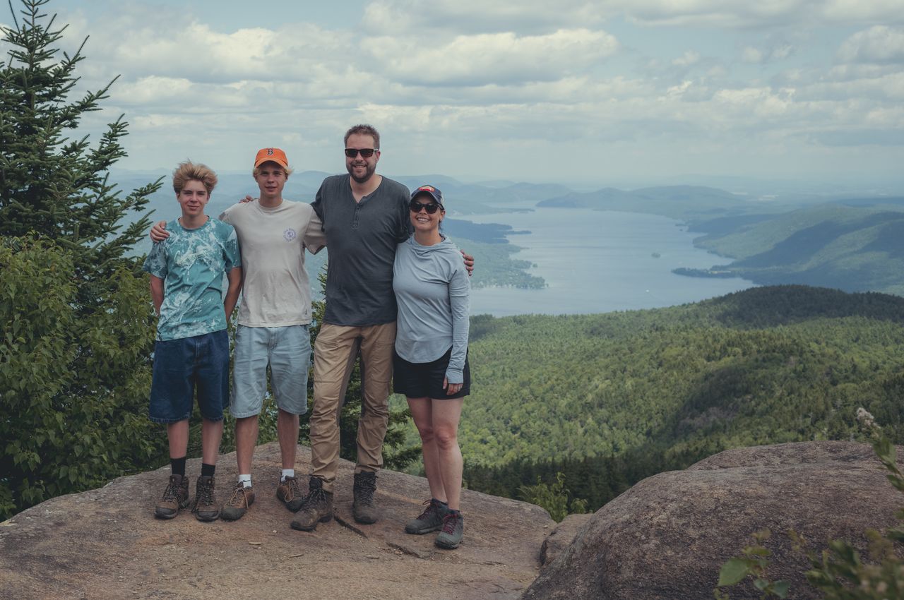 Family of four posing on a mountain summit overlooking a lake.