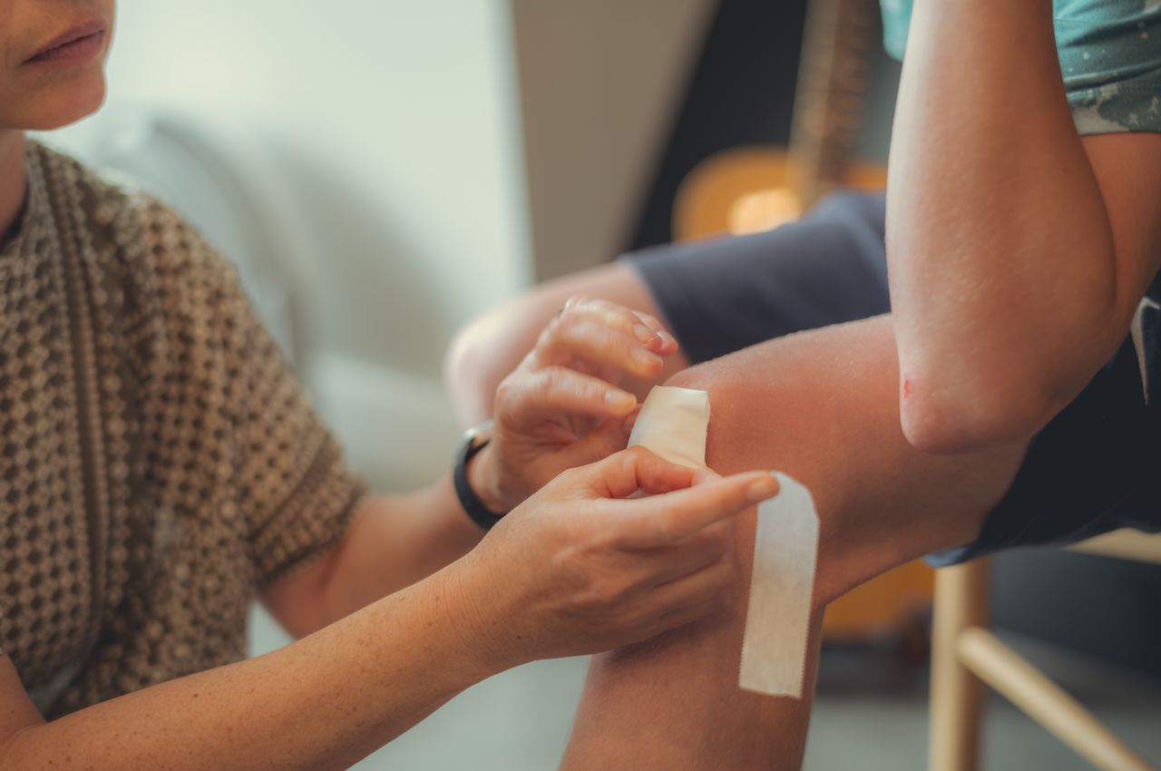 A woman applying a bandage to a boy's knee.