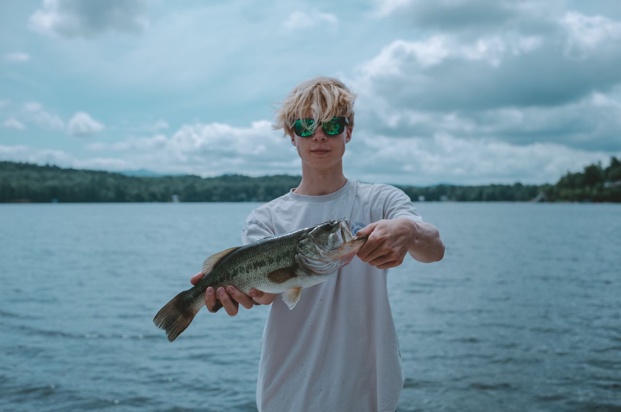 A young man holding up his freshly caught fish.