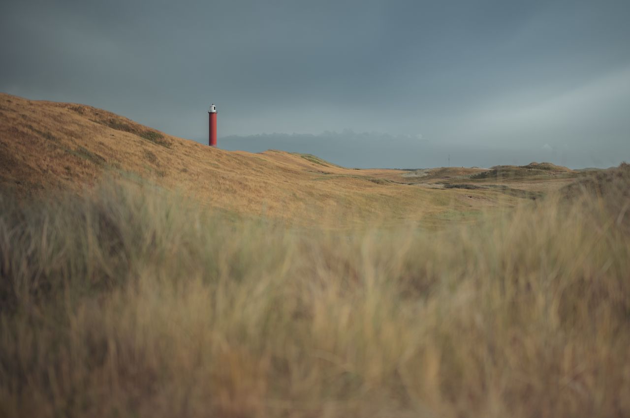 A red lighthouse standing tall in the dunes.