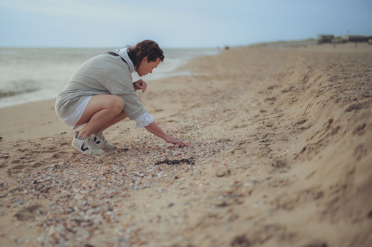 A woman on a beach searching for seashells.