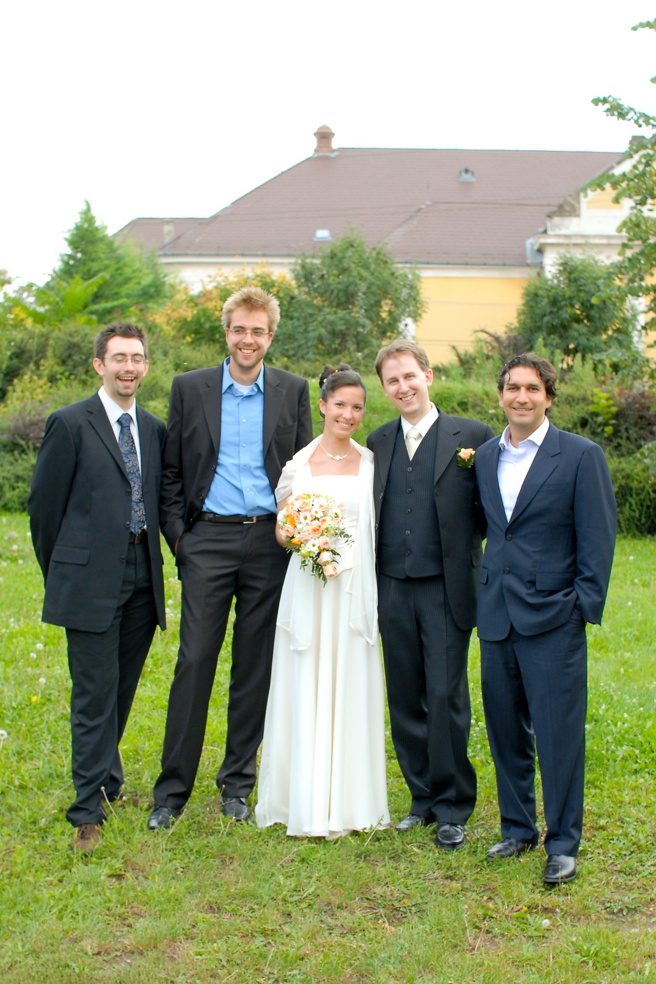 The bride and groom stand outdoors with three men in suits, smiling for a wedding photo.