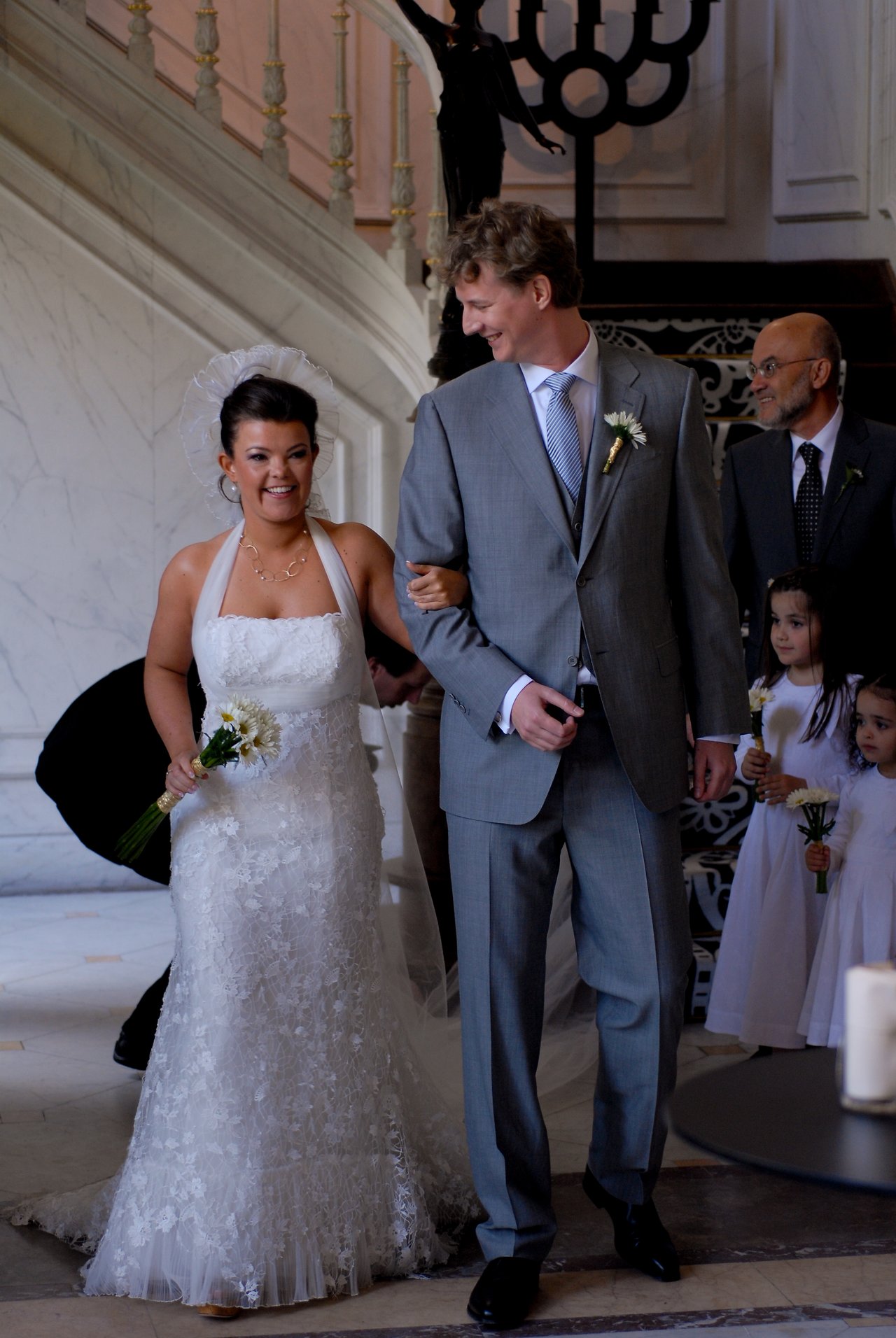 The bride and groom walk arm in arm, smiling, as they head toward the altar with flower girls nearby.