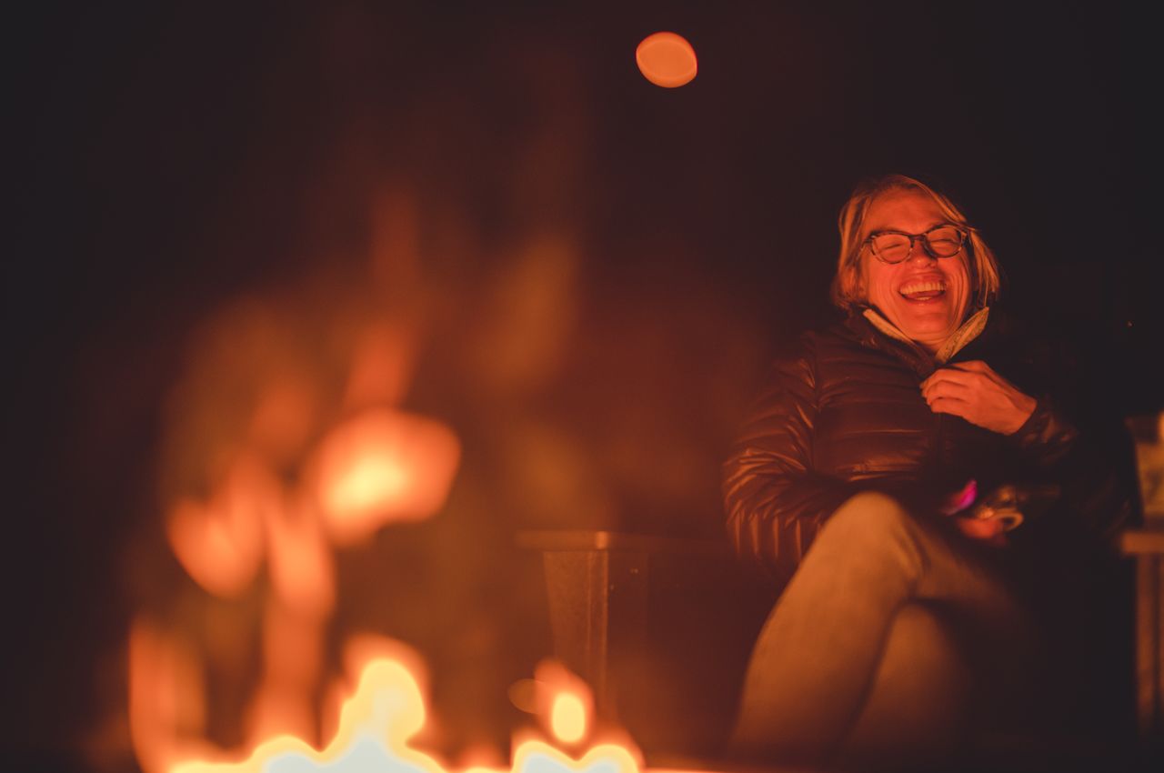 A woman laughing in the glow of a campfire.