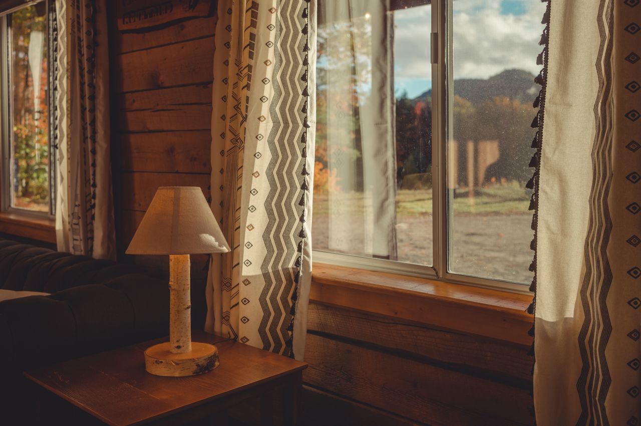 A rental cabin with walls made out of wood, basic curtains, and nice fall light coming through the window.