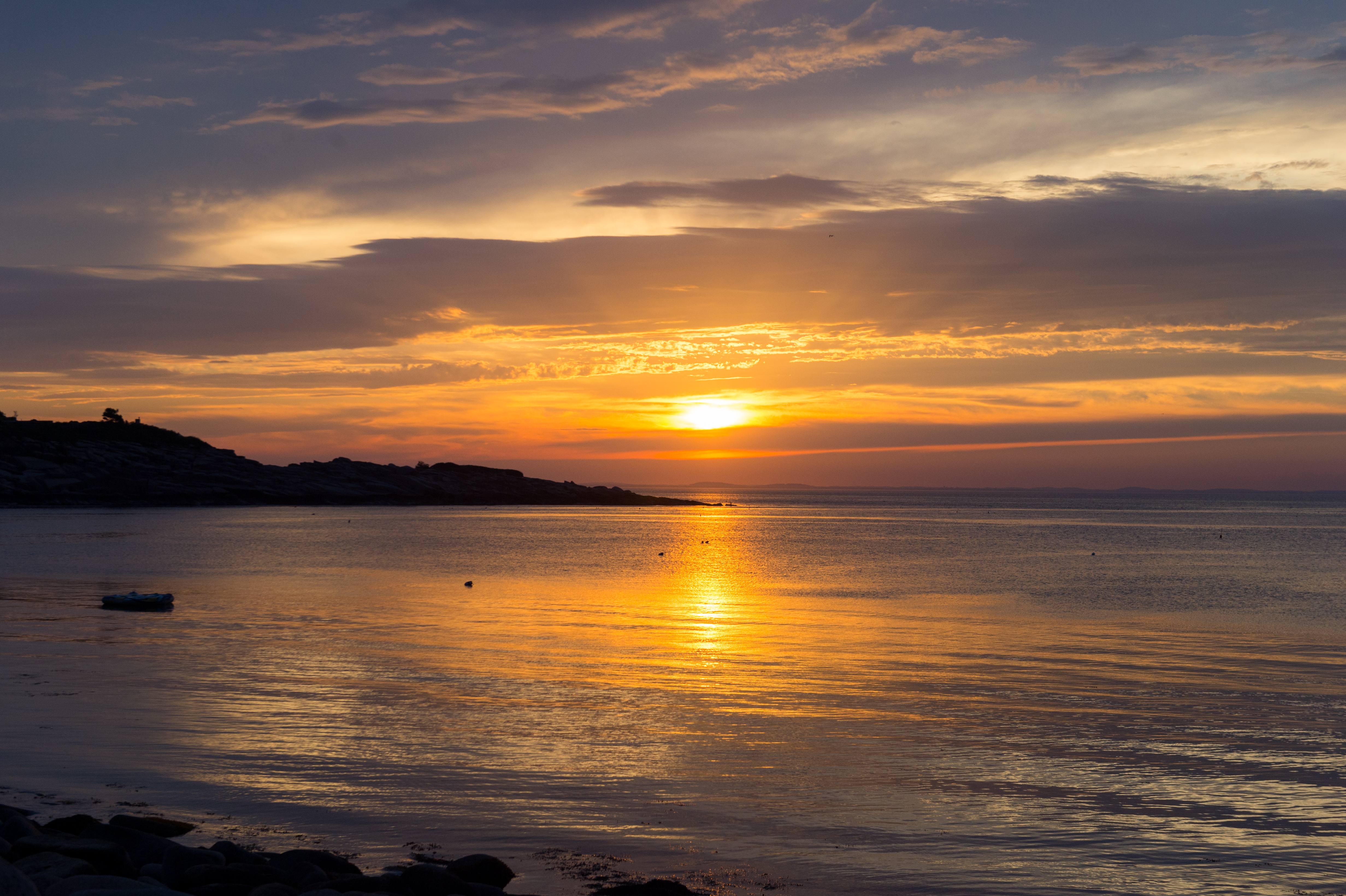 The sun sets over calm coastal waters, casting a golden reflection.
