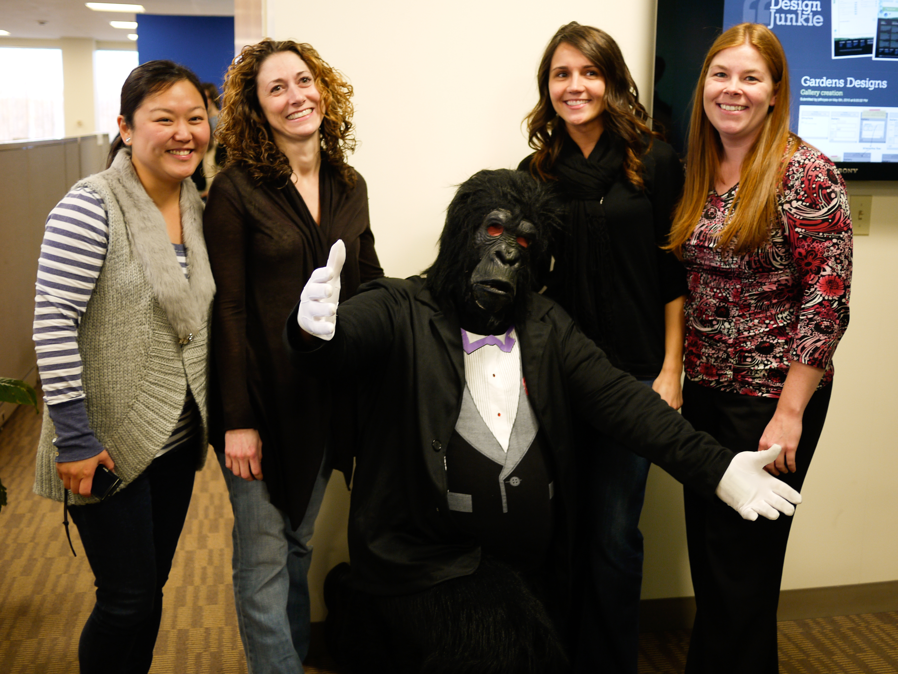 Four women pose with a person in a gorilla costume wearing a tuxedo, who is giving a thumbs-up.