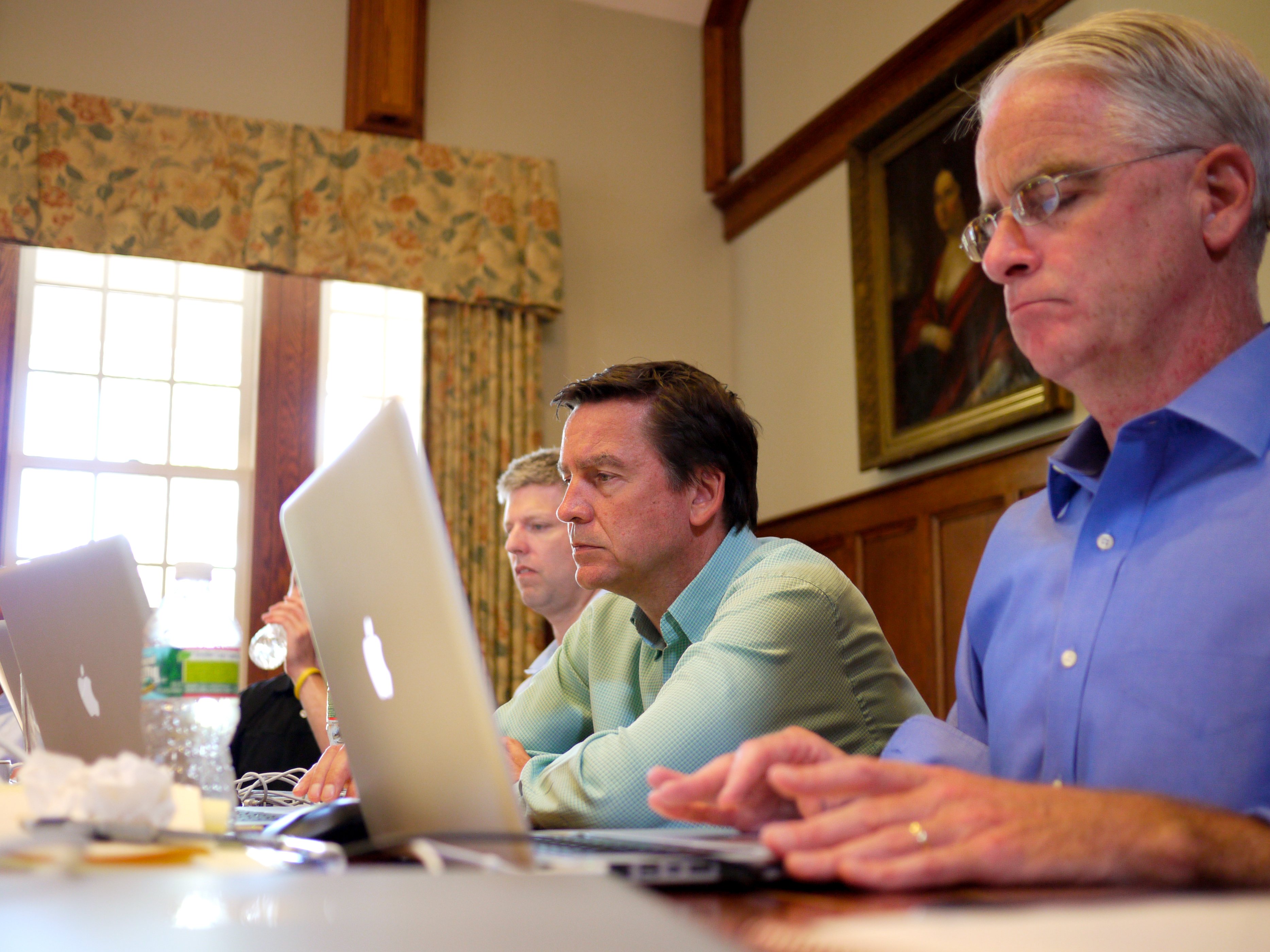 People in a meeting room working on laptops, engaged in discussion during a leadership offsite event.