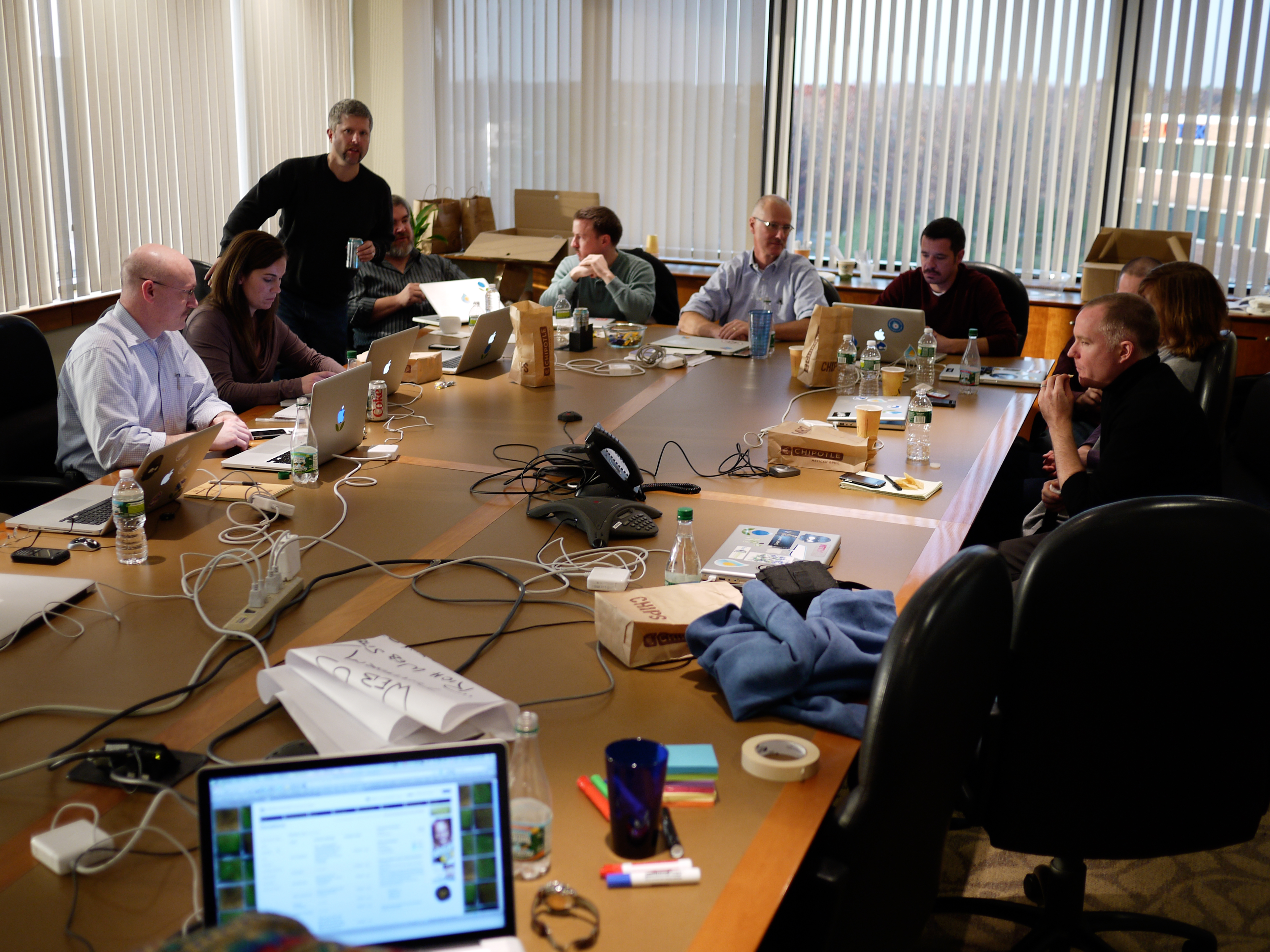 A group of people in a conference room working on laptops and discussing during a leadership offsite meeting.