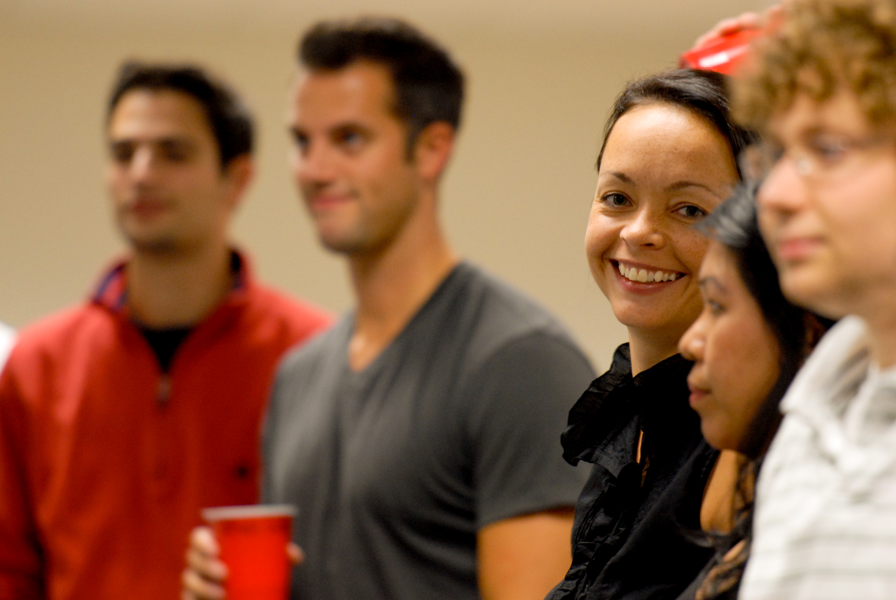 A woman in a black top is smiling while standing among a group of people at a gathering.