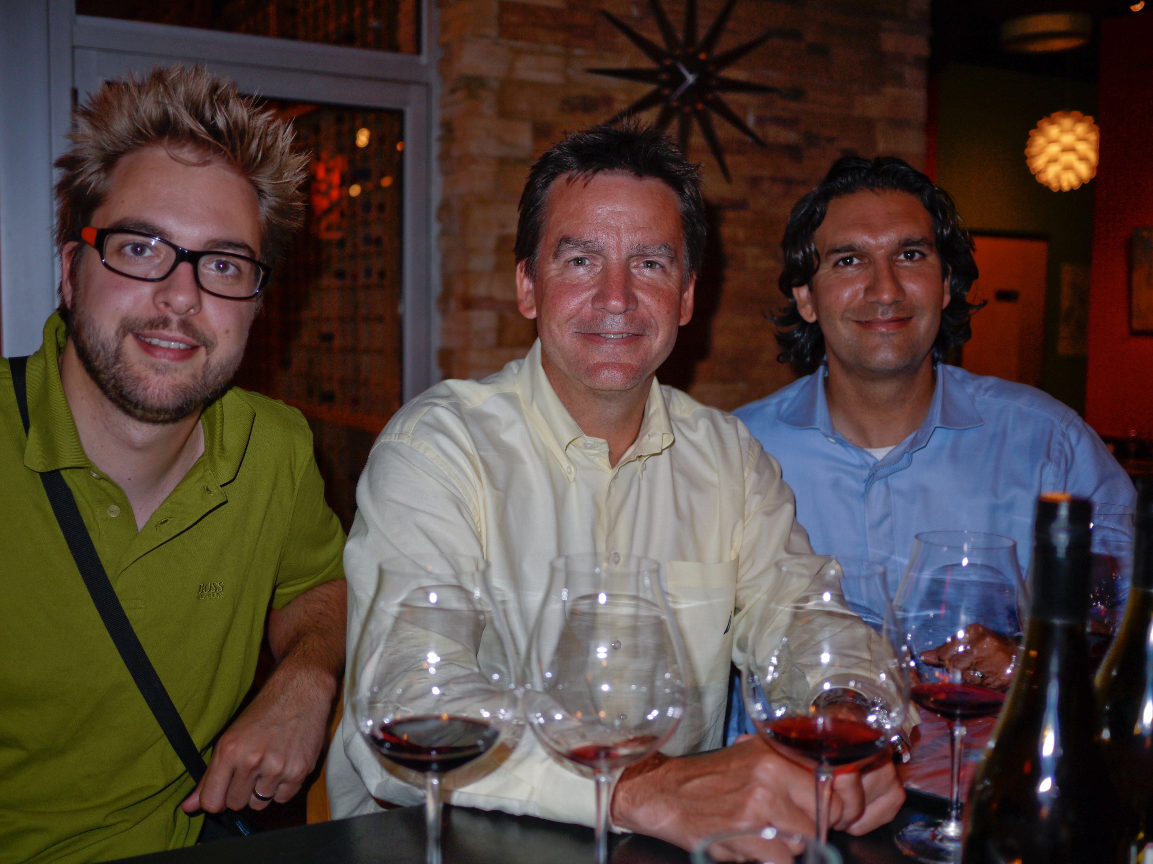 Three men sitting at a table with wine glasses, participating in a wine tasting event in Portland.