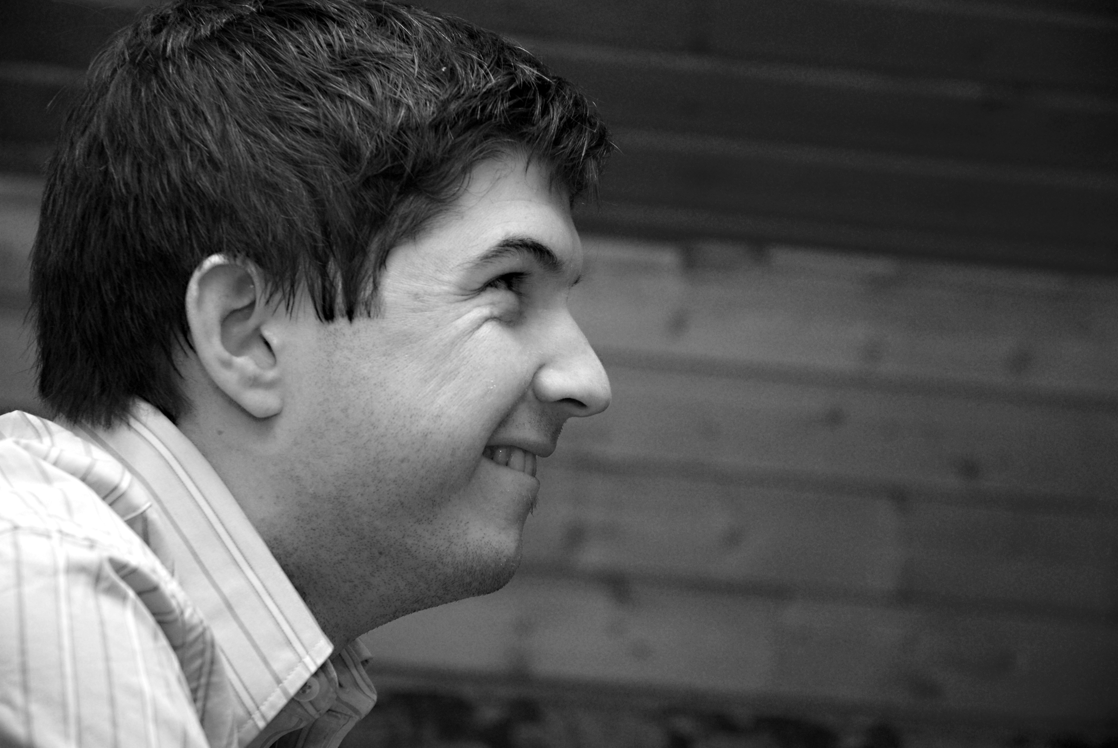 A man in a striped shirt smiles while looking to the side in a black-and-white photo.
