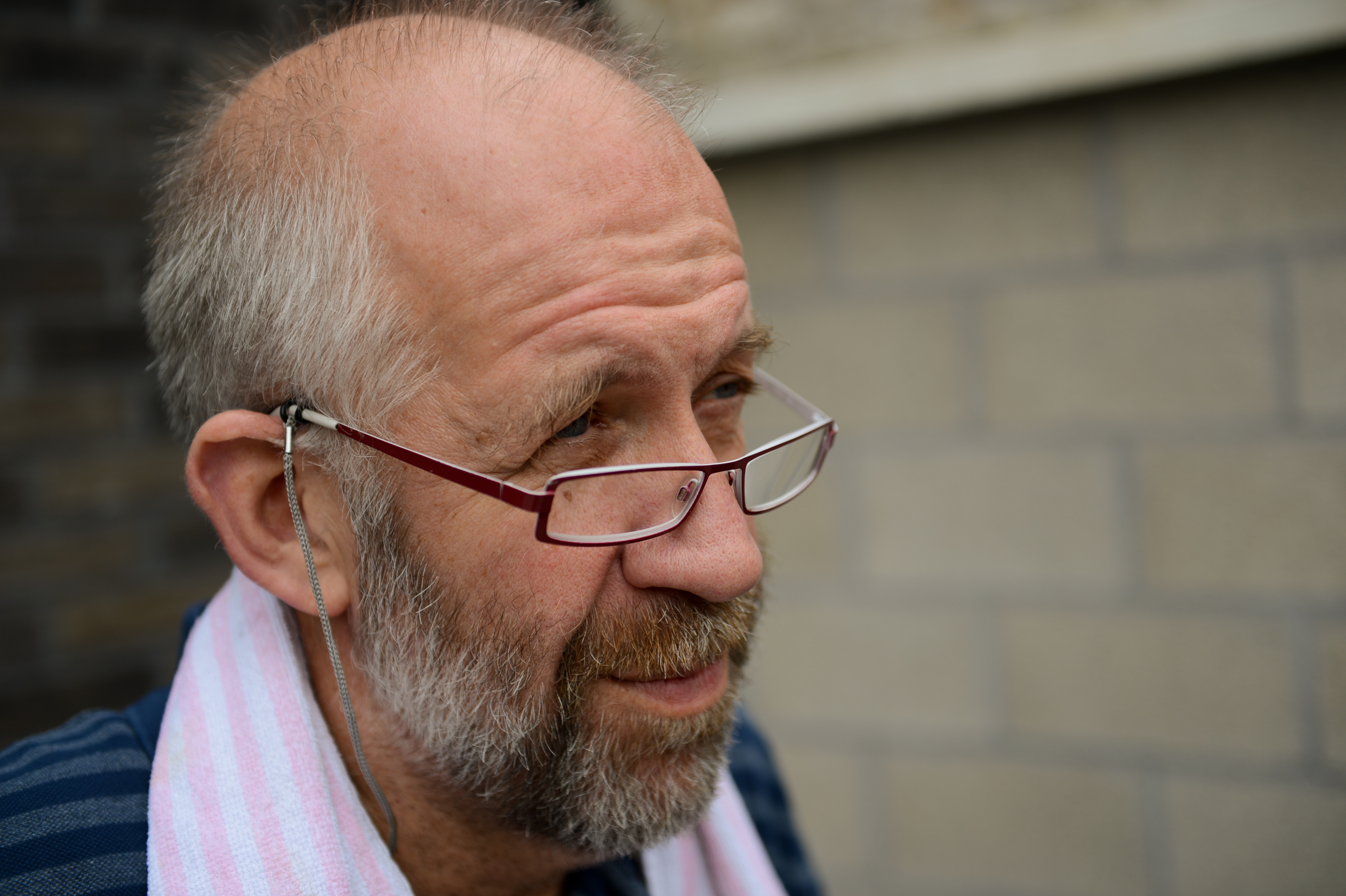 A man with glasses and a beard looks off to the side, wearing a striped towel over his shoulder.
