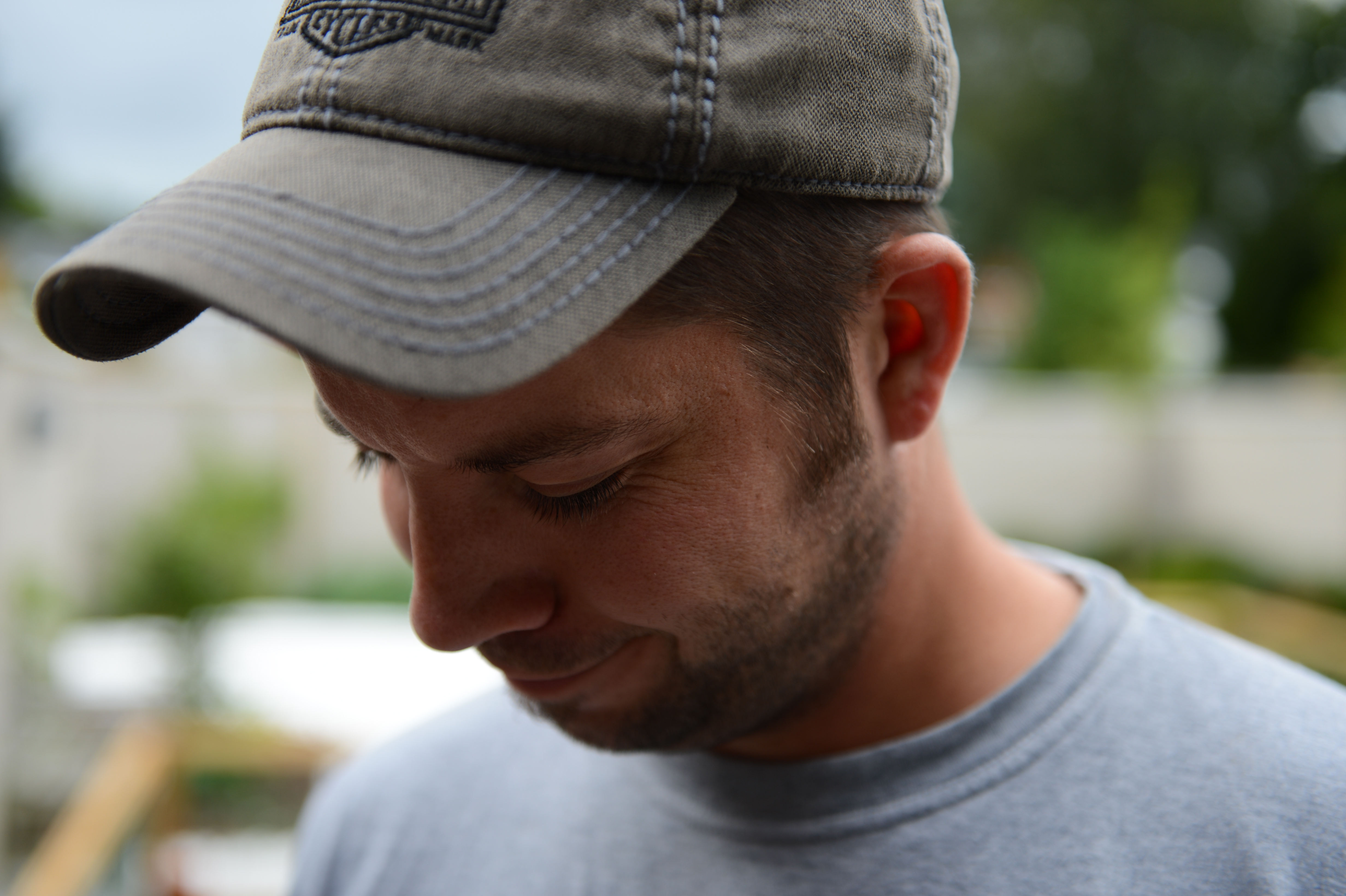 A man wearing a gray cap and shirt looks downward with a slight smile.