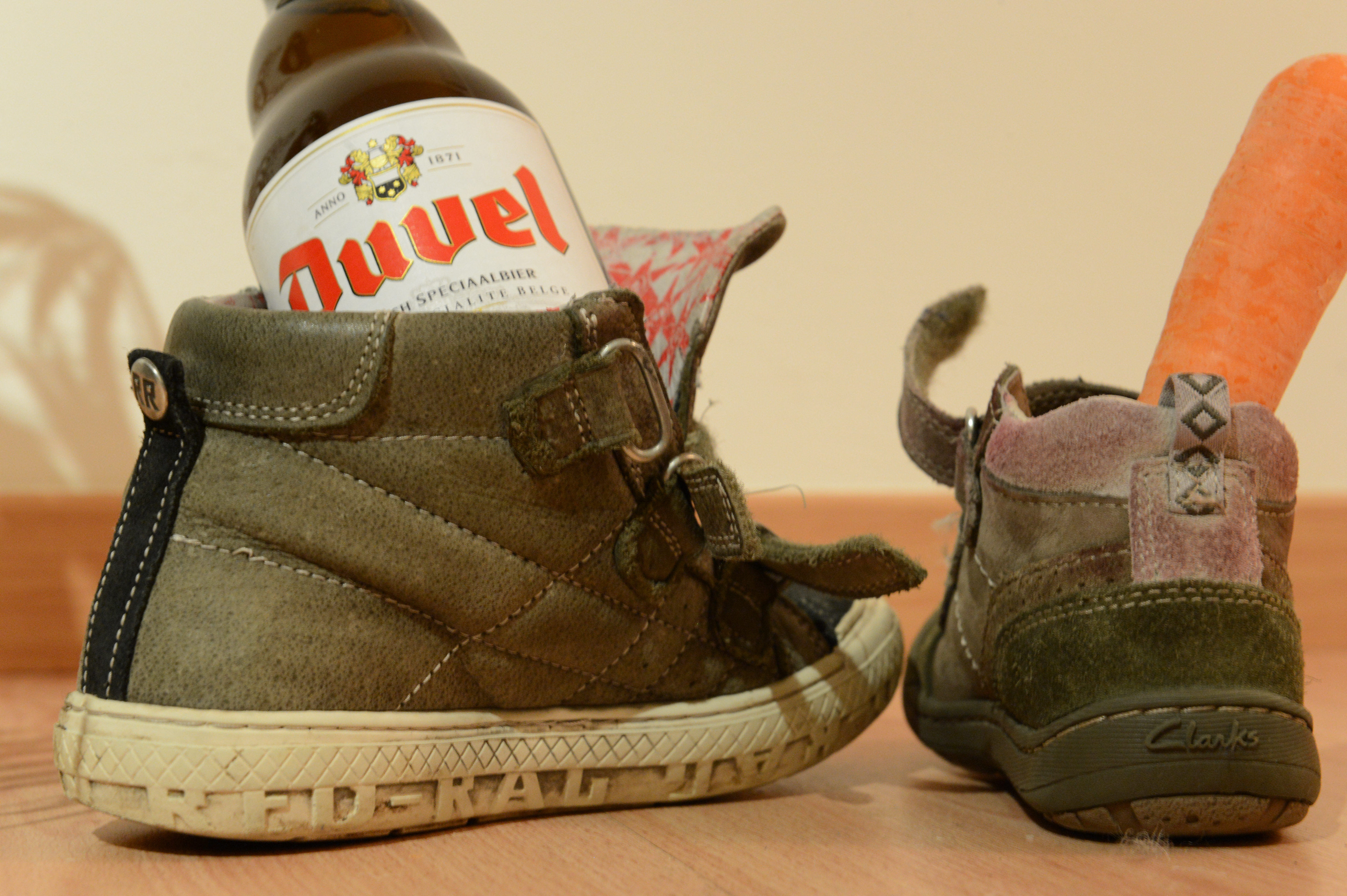 Two children's shoes on the floor, one holding a beer bottle and the other a carrot for Sinterklaas.
