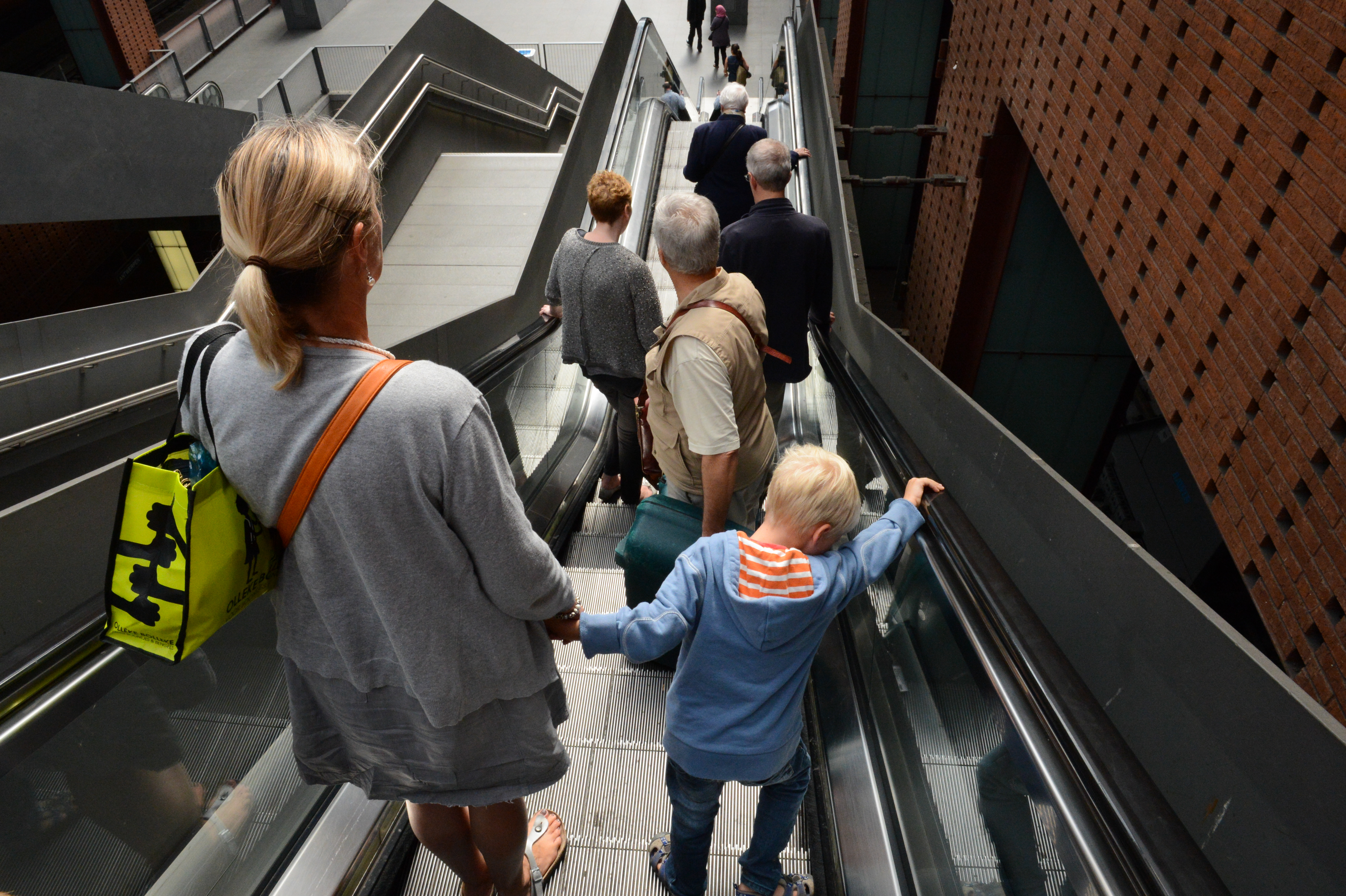 A woman and a child hold hands while descending an escalator with other people.
