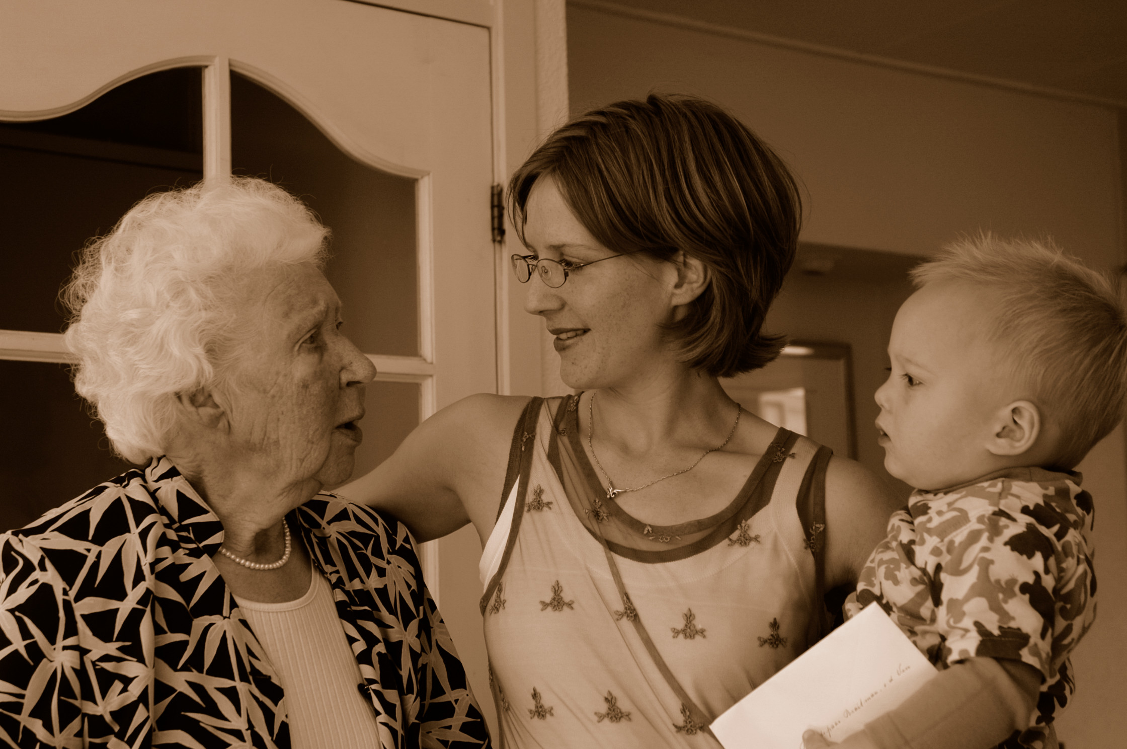 A woman holding a baby talks with an elderly woman, who is looking at her attentively.
