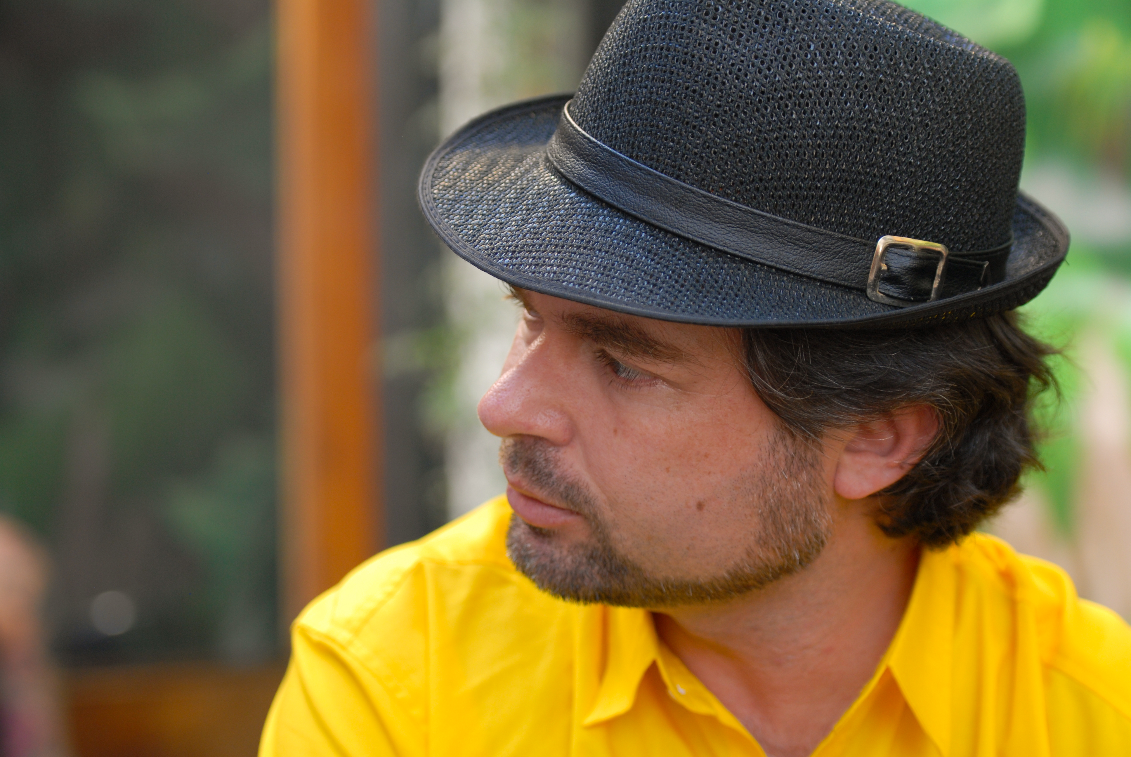 A man in a black hat and yellow shirt looks to the side at a party.