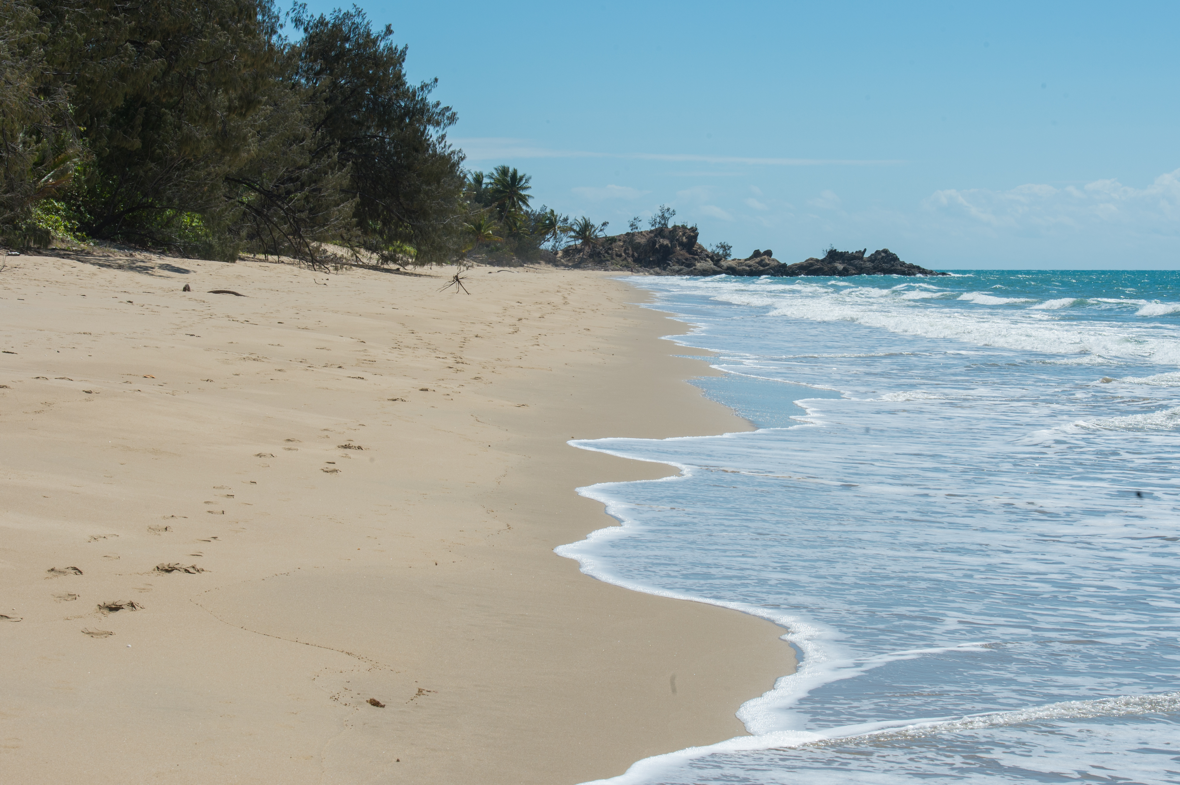 Waves wash onto a sandy beach, leaving a trail of footprints near the water's edge.