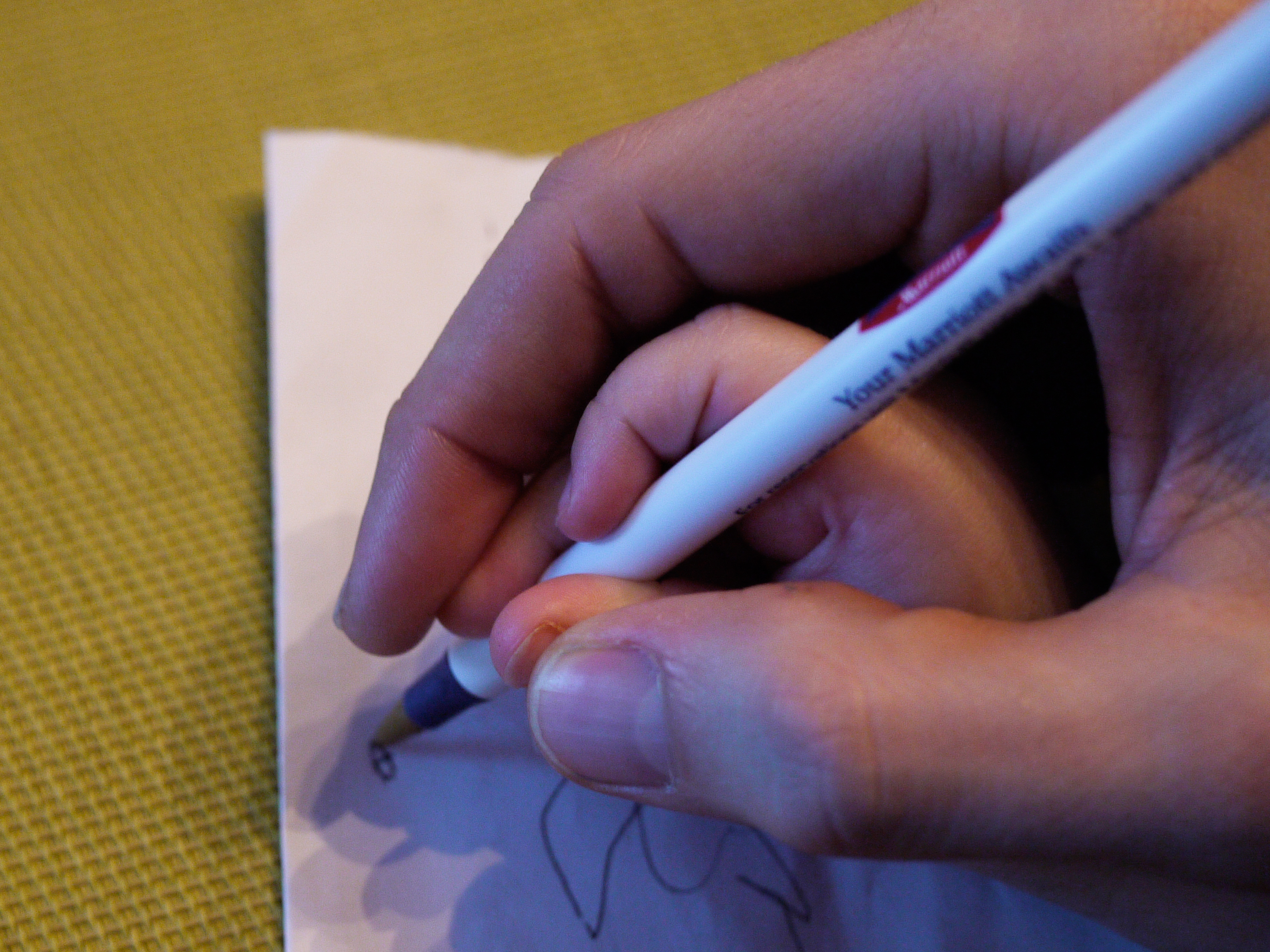 An adult hand guides a child&#039;s small hand in holding a pen and writing on a piece of paper.