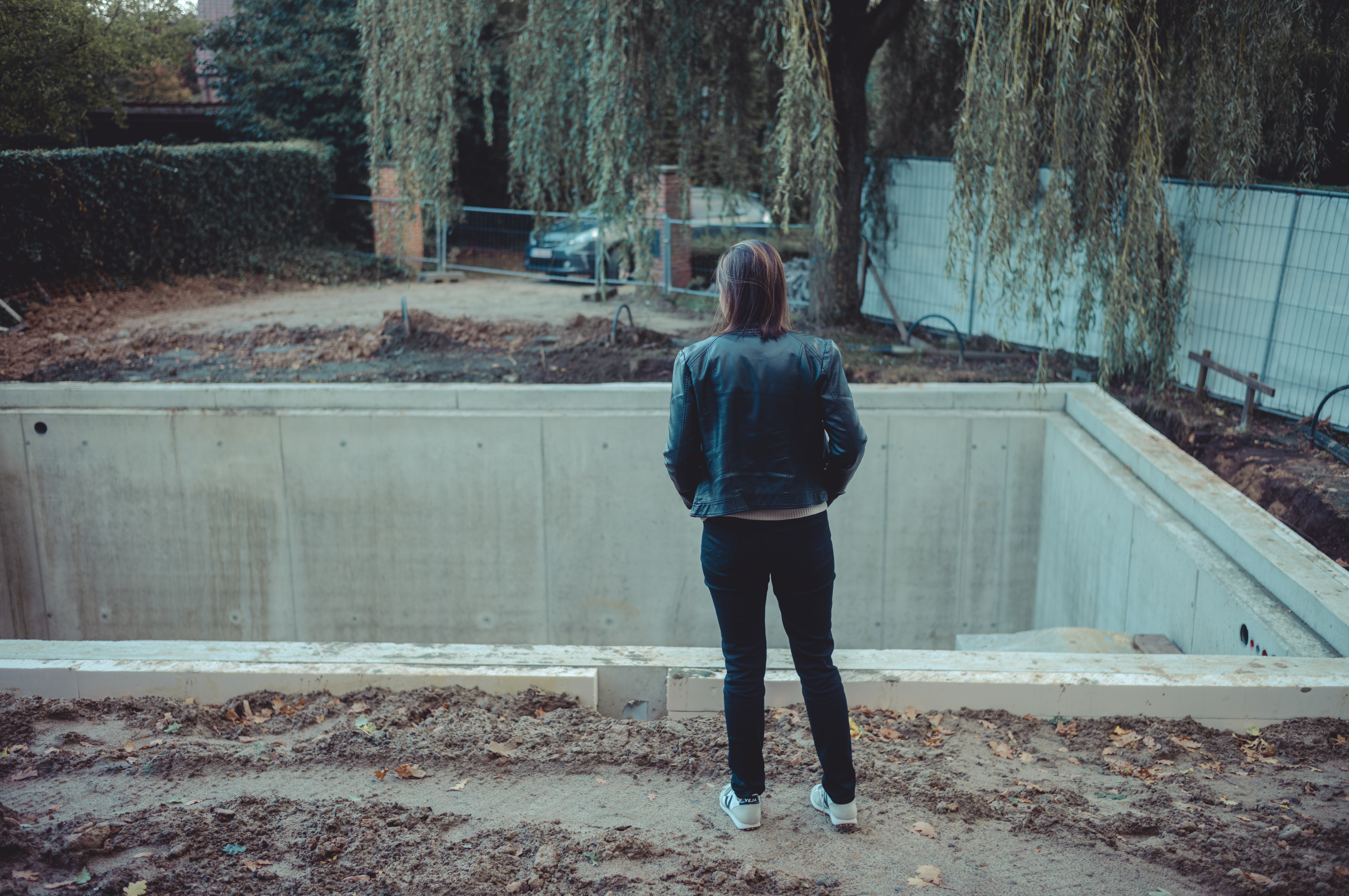 A person in a black jacket stands at the edge of a concrete basement under construction for a future garage.