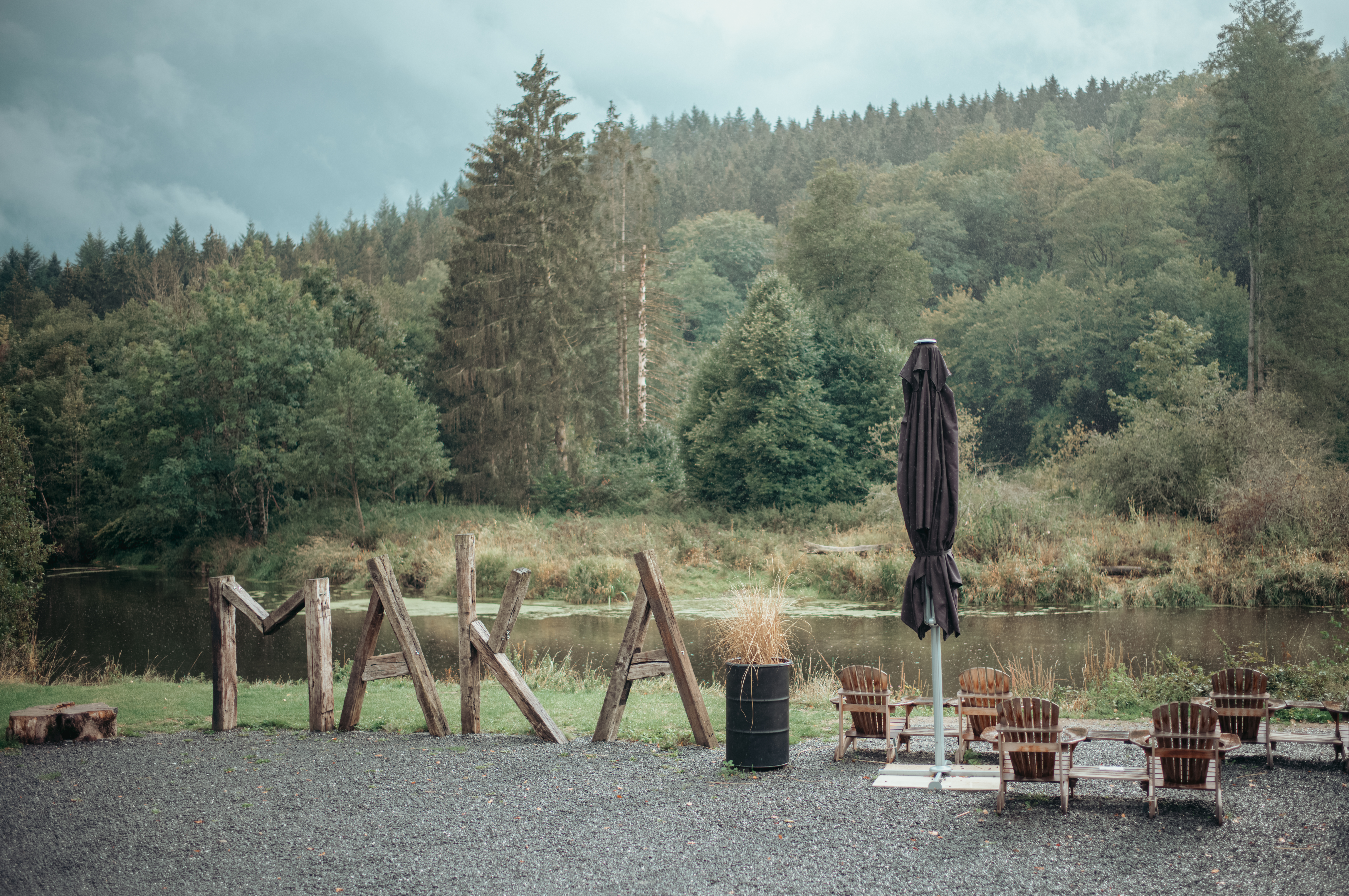 The word &#039;Maka&#039; spelled with large logs, standing next to a river.