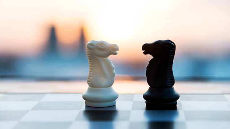 Two chess knights, one white and one black, face each other on a board, symbolizing competition and collaboration.