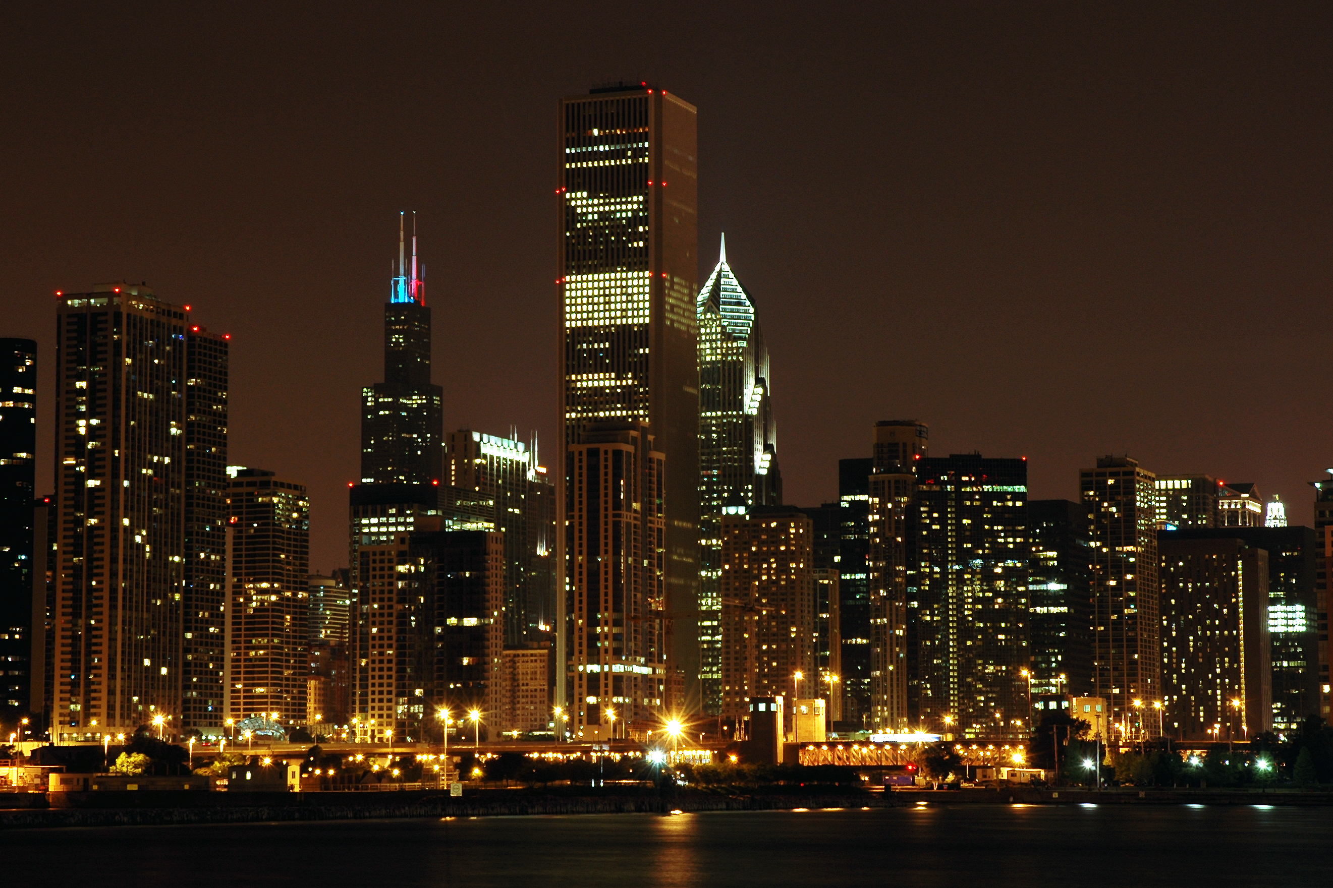 Chicago skyline at night with illuminated skyscrapers and city lights reflecting on the water.