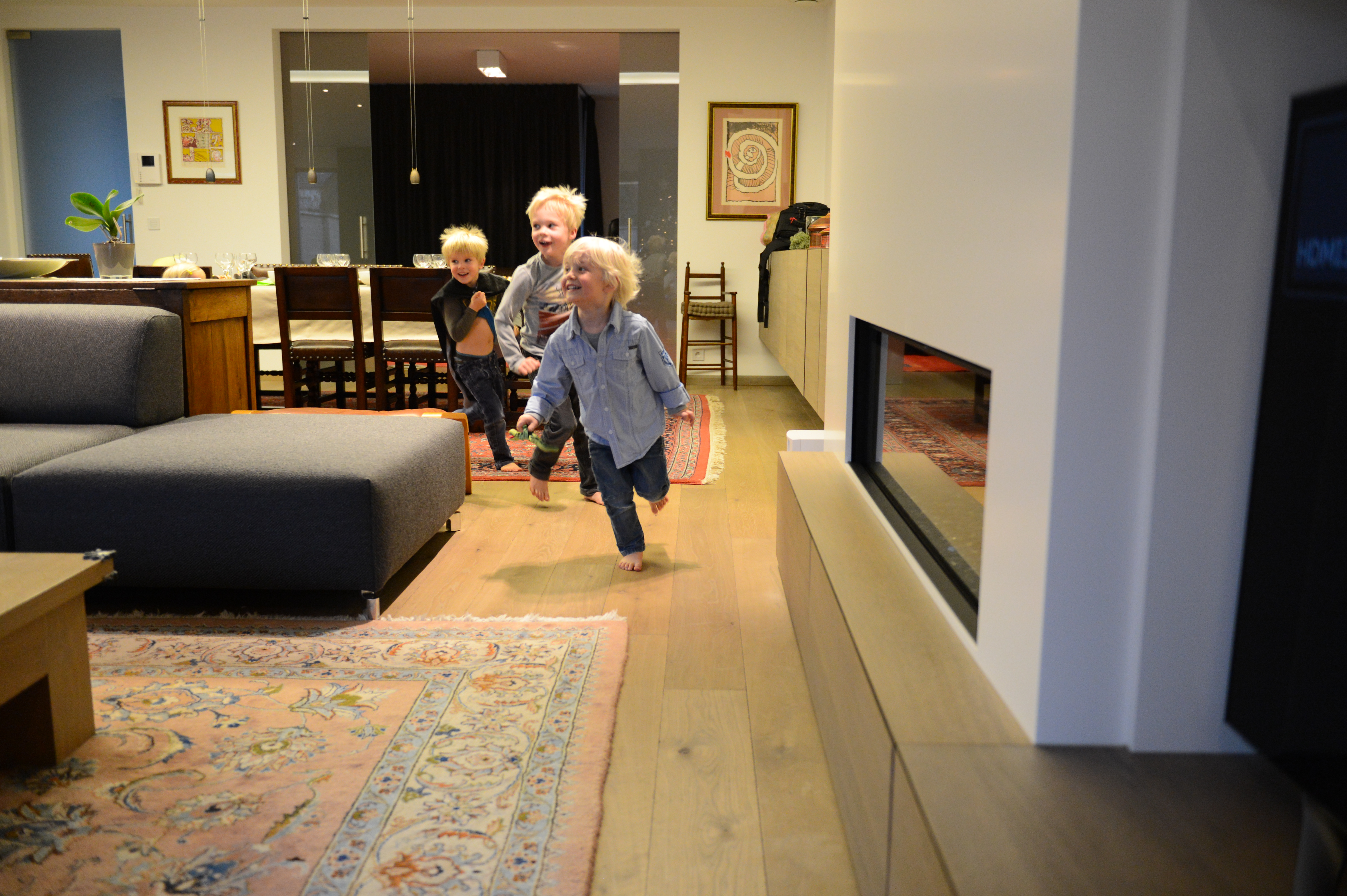 Three young children run barefoot through a warmly lit living room, smiling and playing together on Christmas Eve.