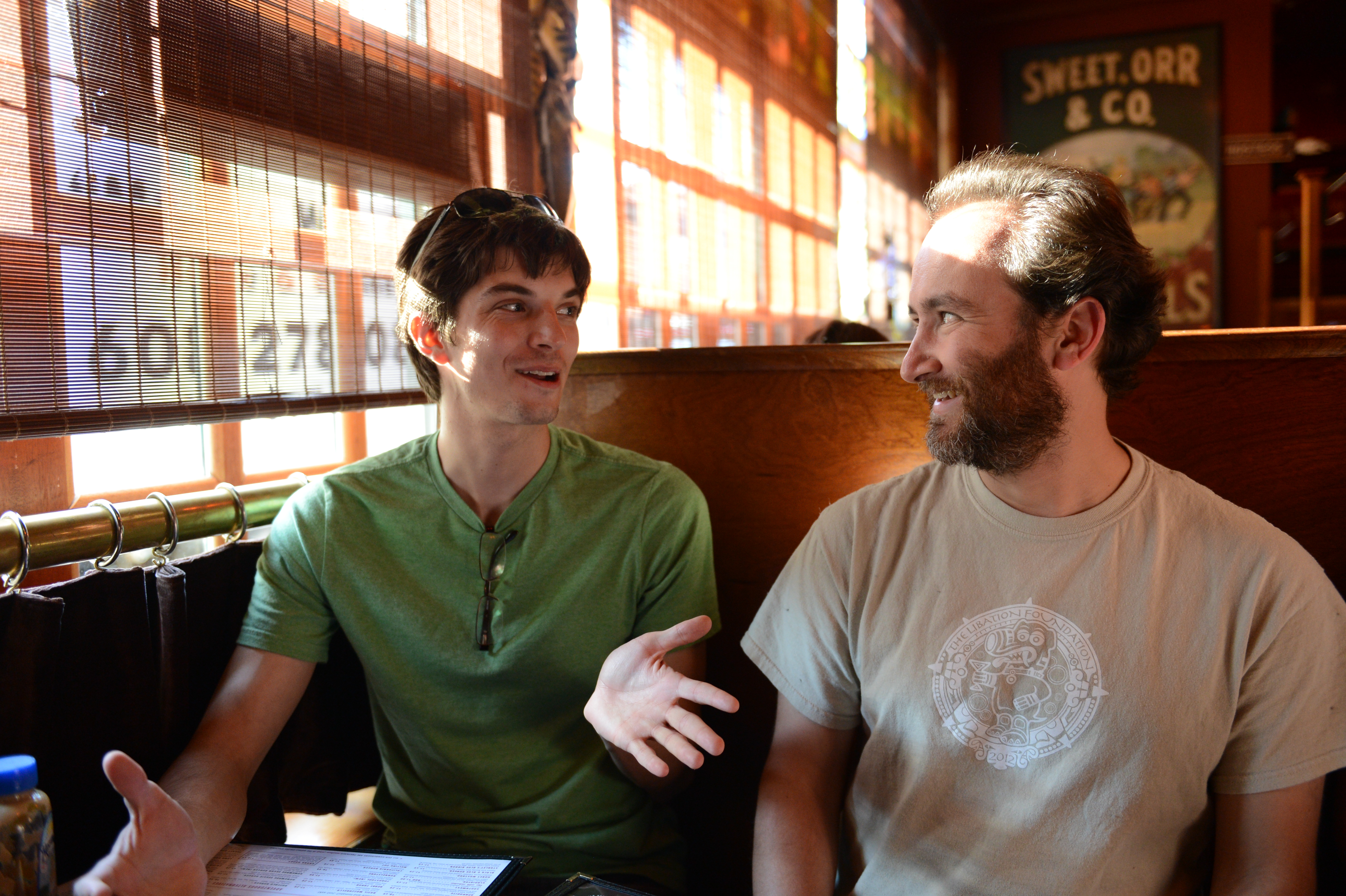 Two people sitting in a booth, engaged in a conversation, with one gesturing while speaking.