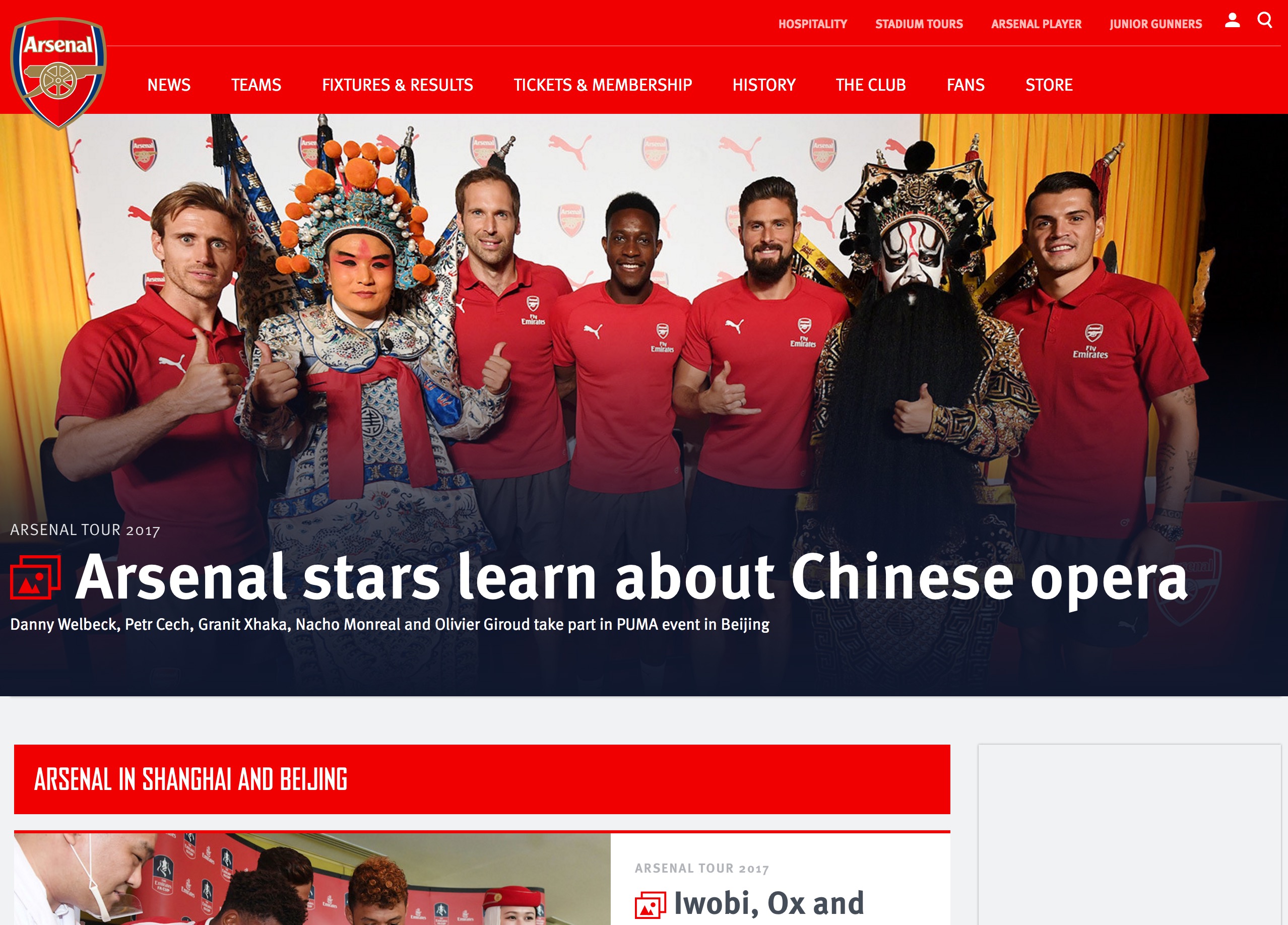 Arsenal players pose with Chinese opera performers at a cultural event in Beijing, wearing team shirts and smiling.