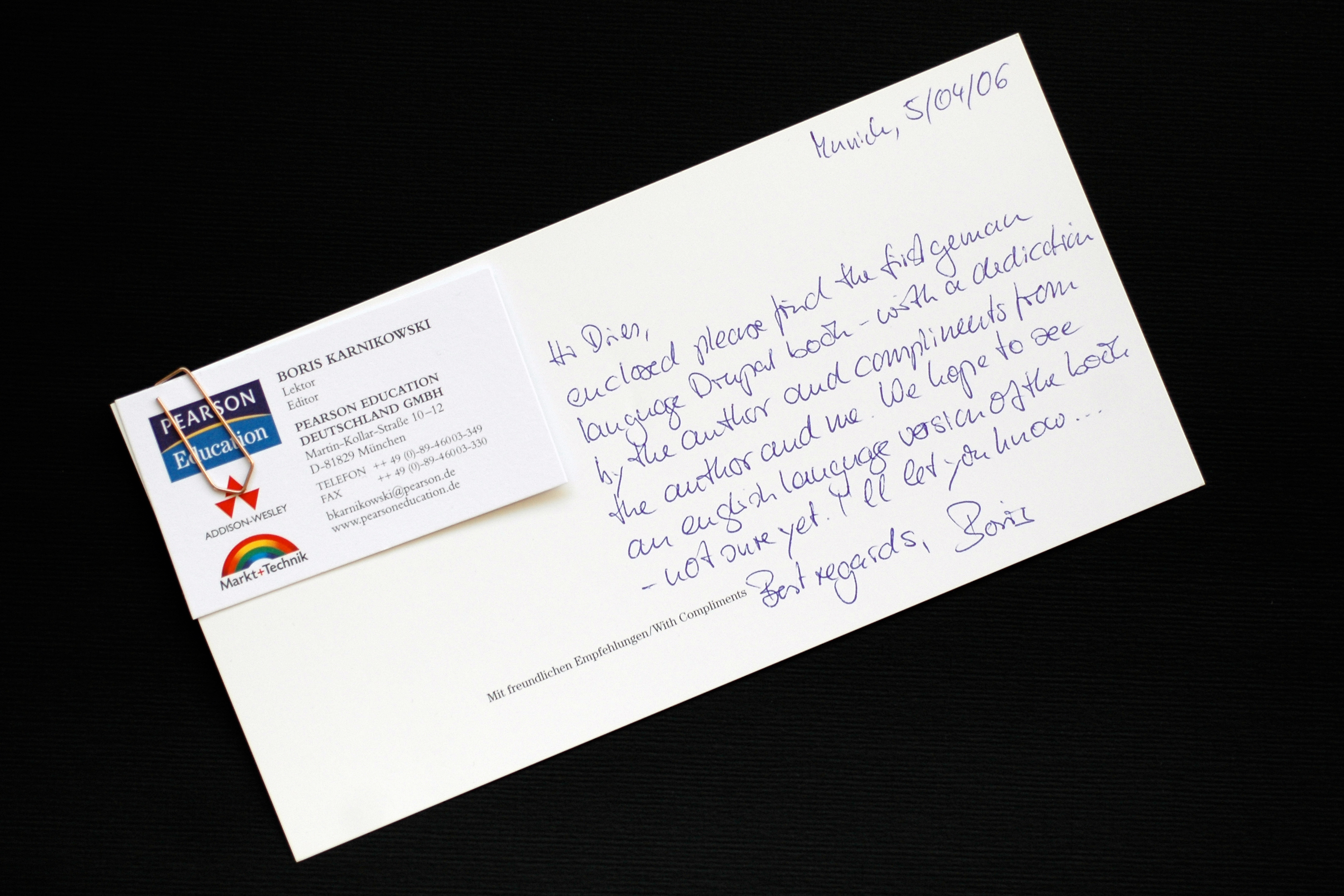 A handwritten note with a business card attached, discussing the first German-language Drupal book and its English version.