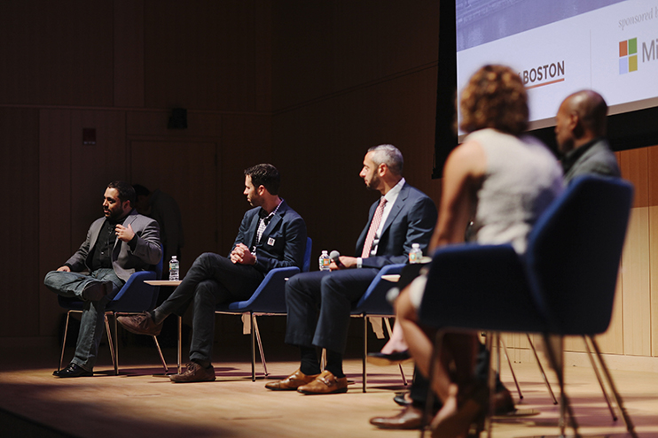 Panelists seated on stage discuss the Boston government launch event, with one speaker gesturing while others listen attentively.