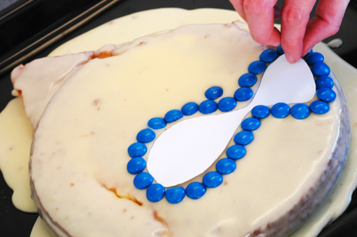 A hand decorating a cake with blue m&m's