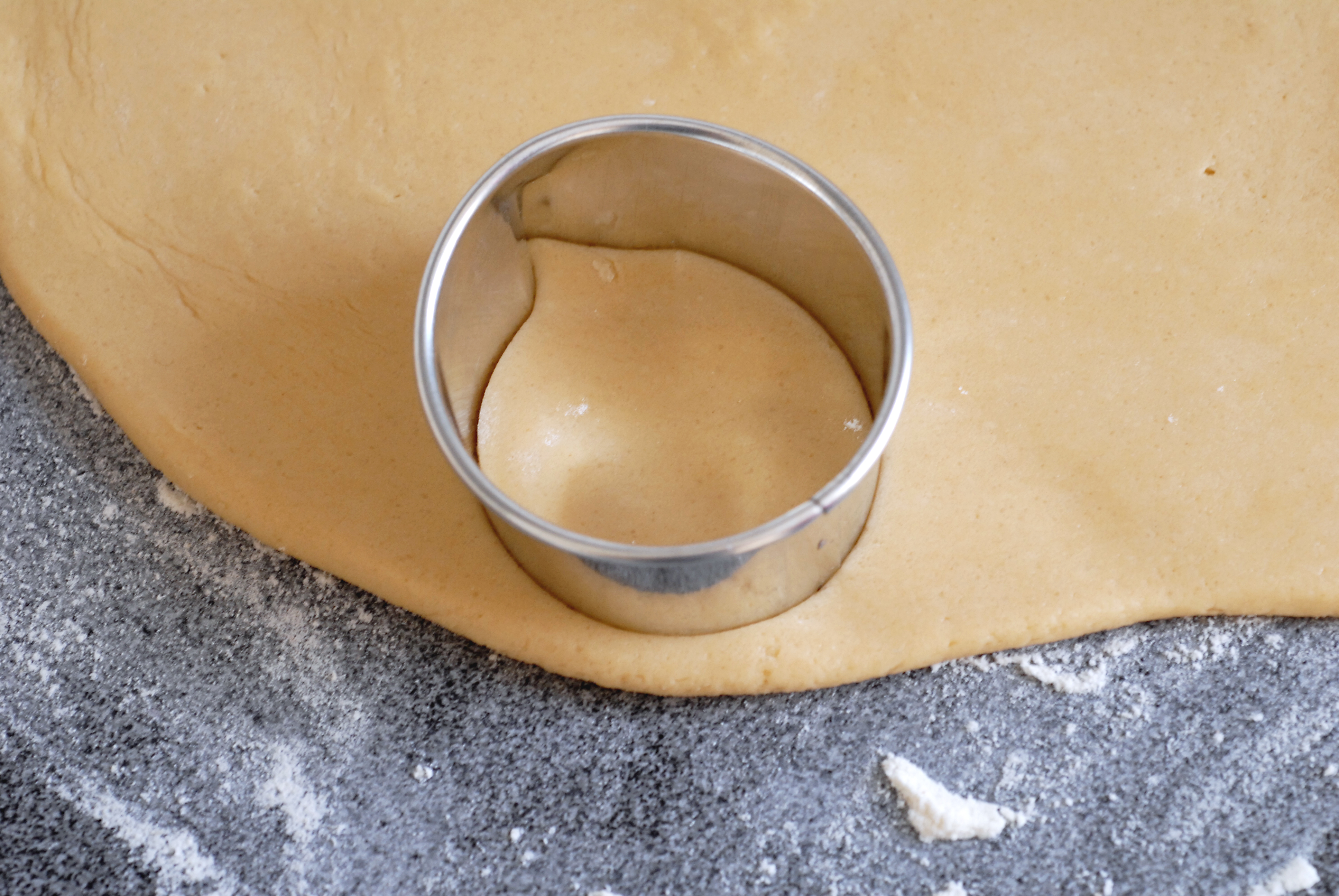 A round cookie cutter is pressed into rolled-out dough on a floured surface.